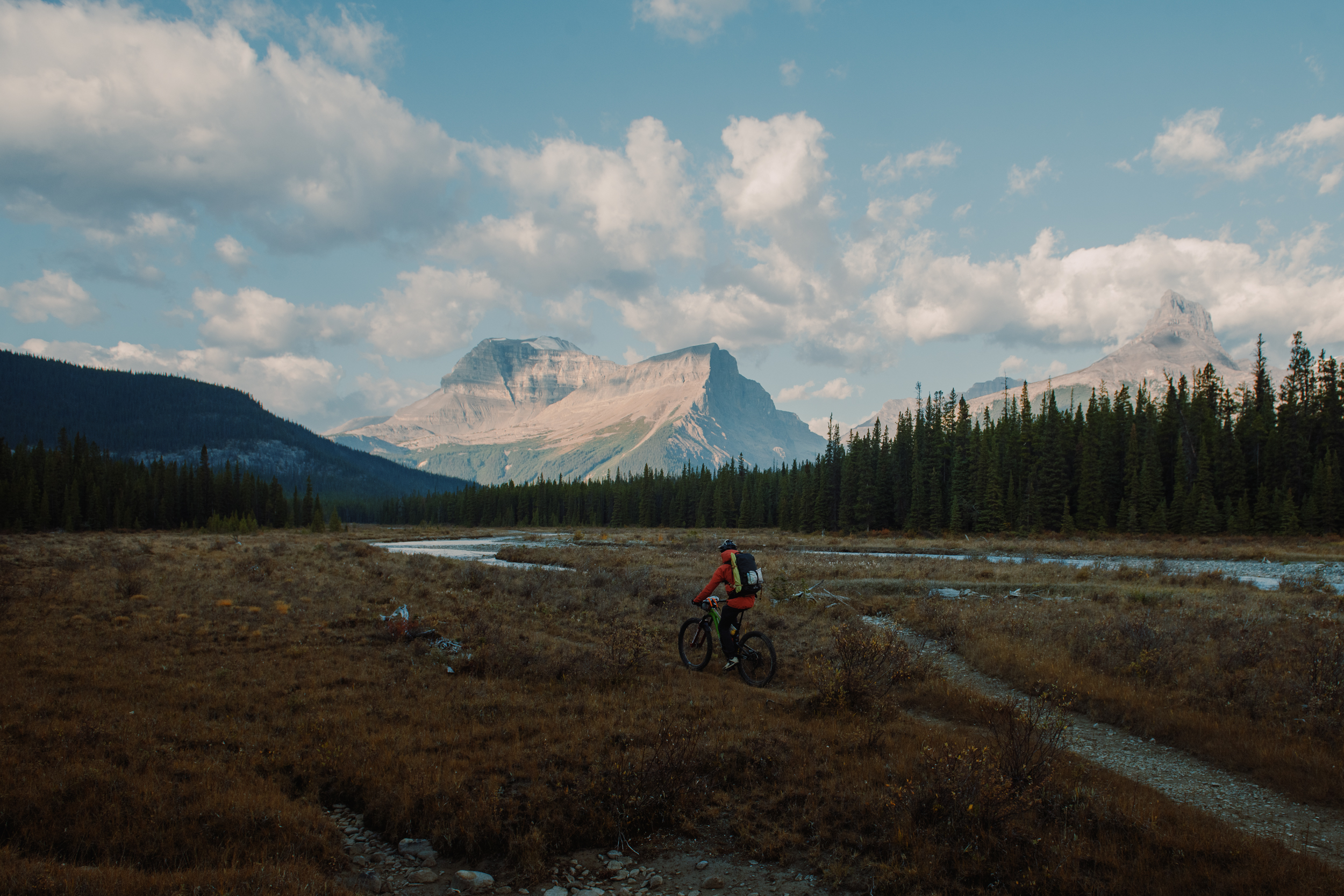 Rider crossing a wide braided river flat below big limestone peaks