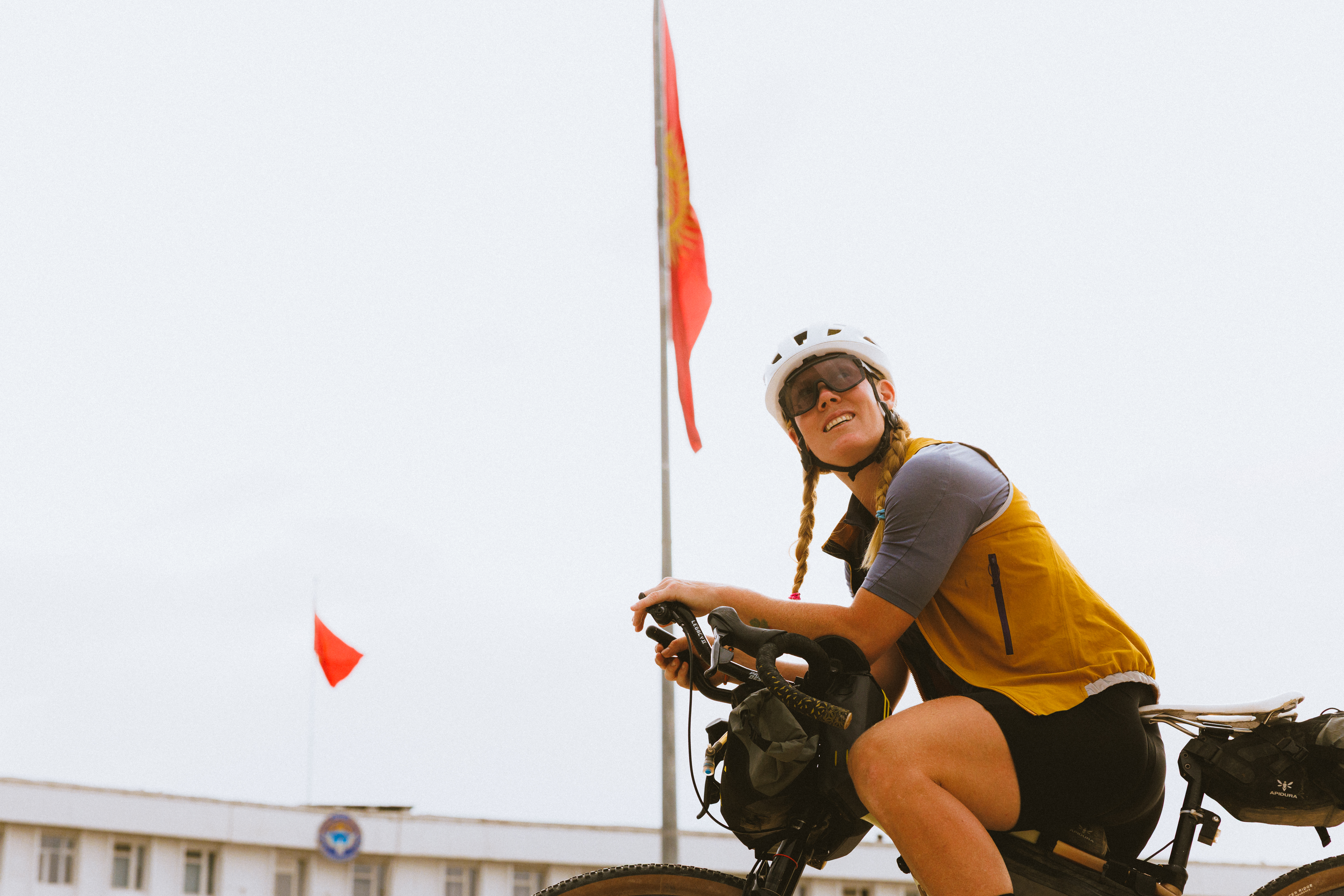 Rider smiling on a loaded bike below a flag against a white sky