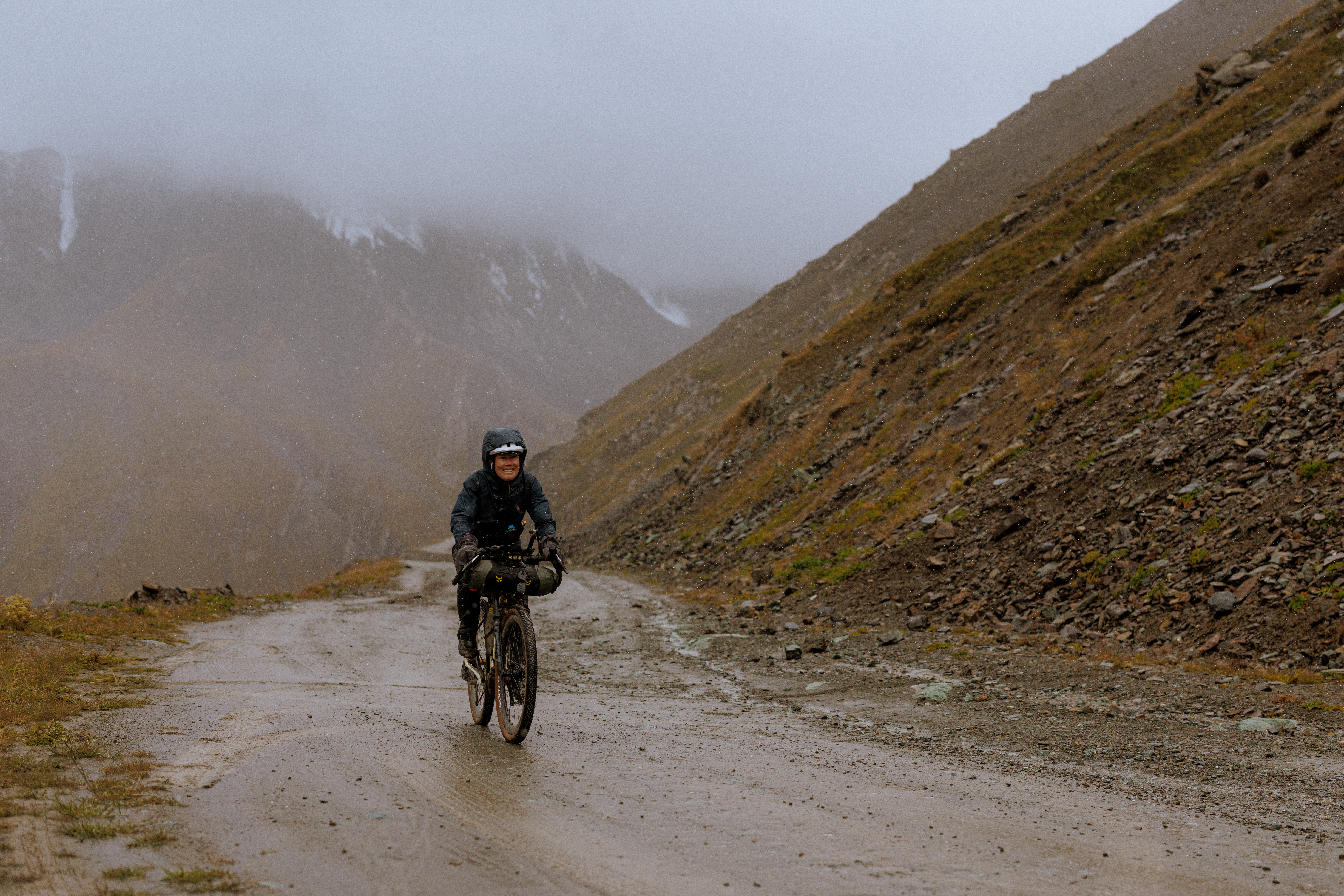 Rider on a wet gravel road climbing into cloud on a bare hillside