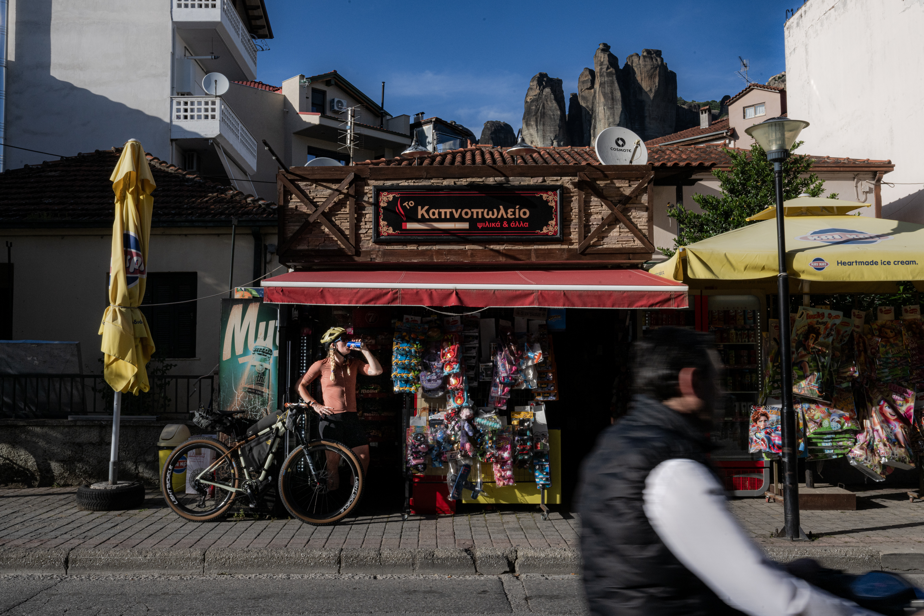 Loaded bike outside a small shop below tall rock towers in a Greek town