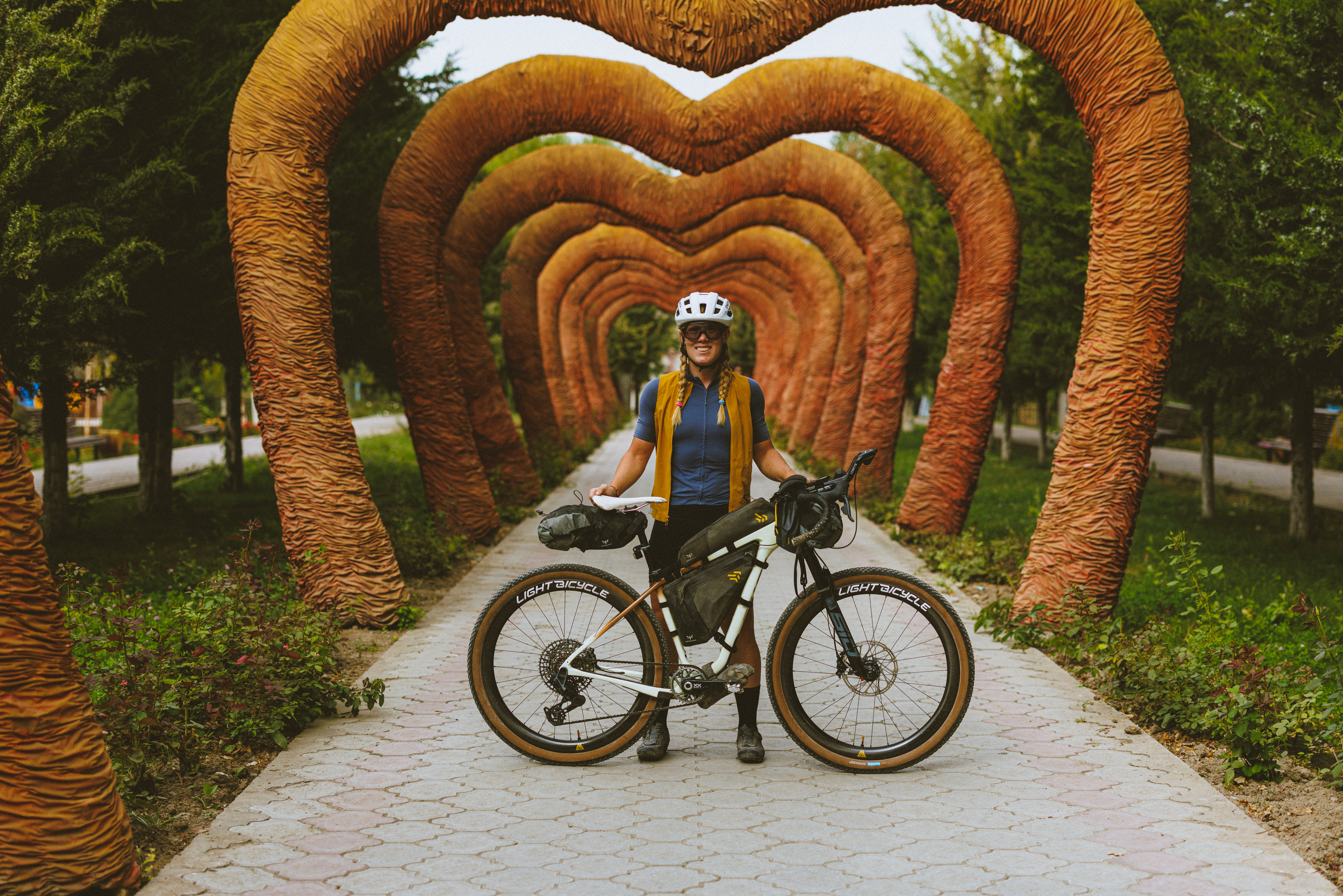 Rider standing with a loaded bike under an arch of shaped tree trunks