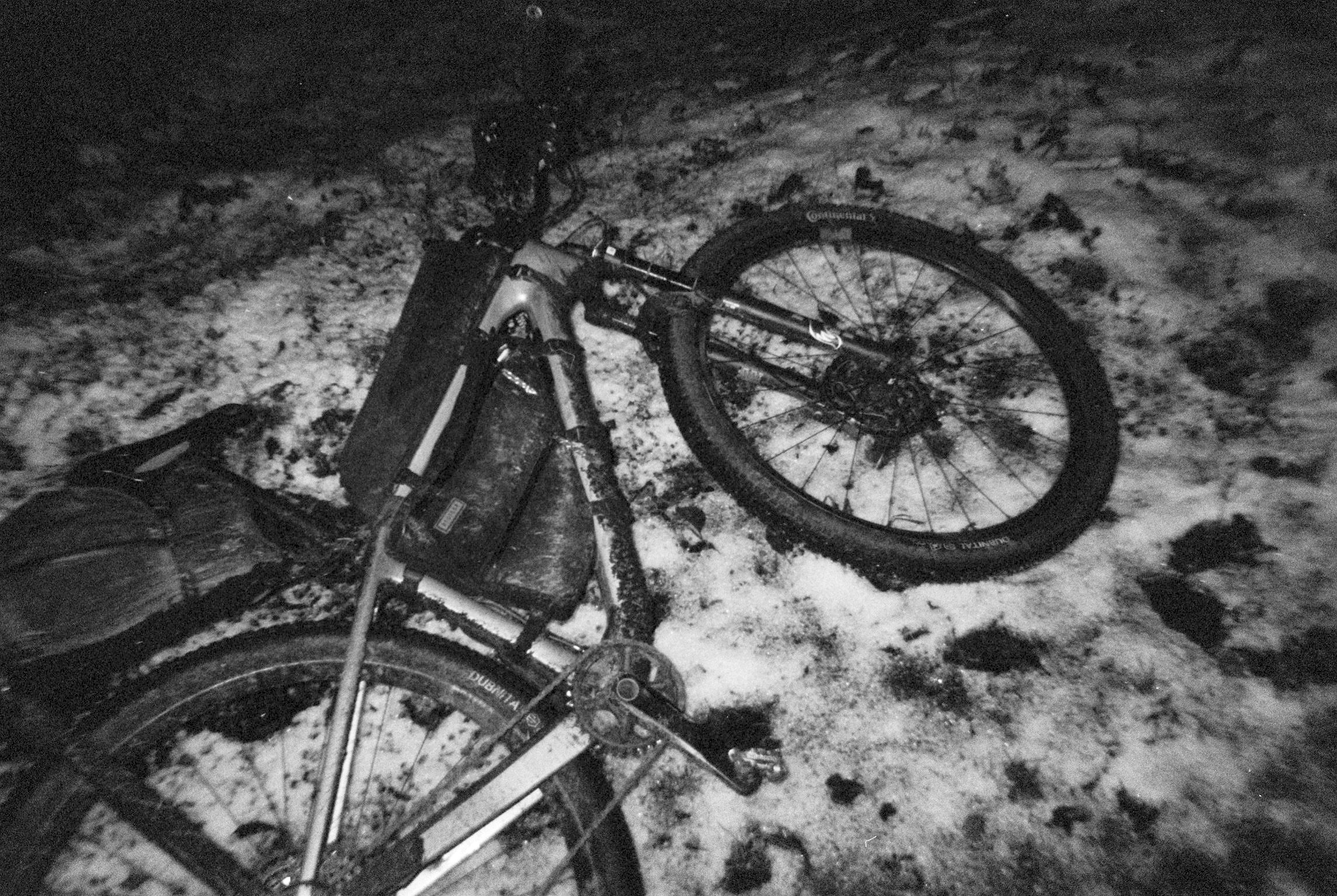 Loaded gravel bike lying on snow-covered ground, black and white