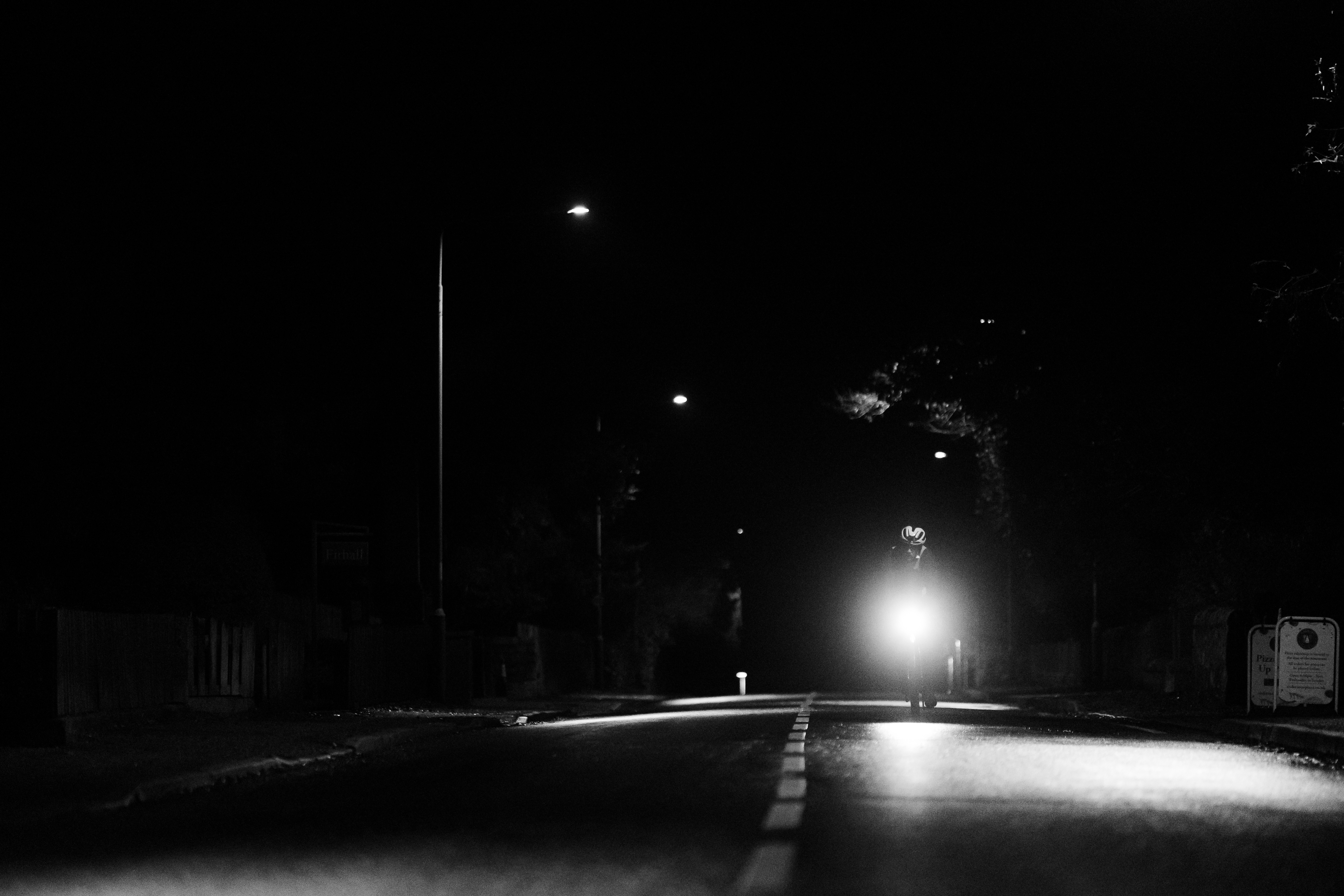 A rider's headlight approaching along a dark road under streetlights
