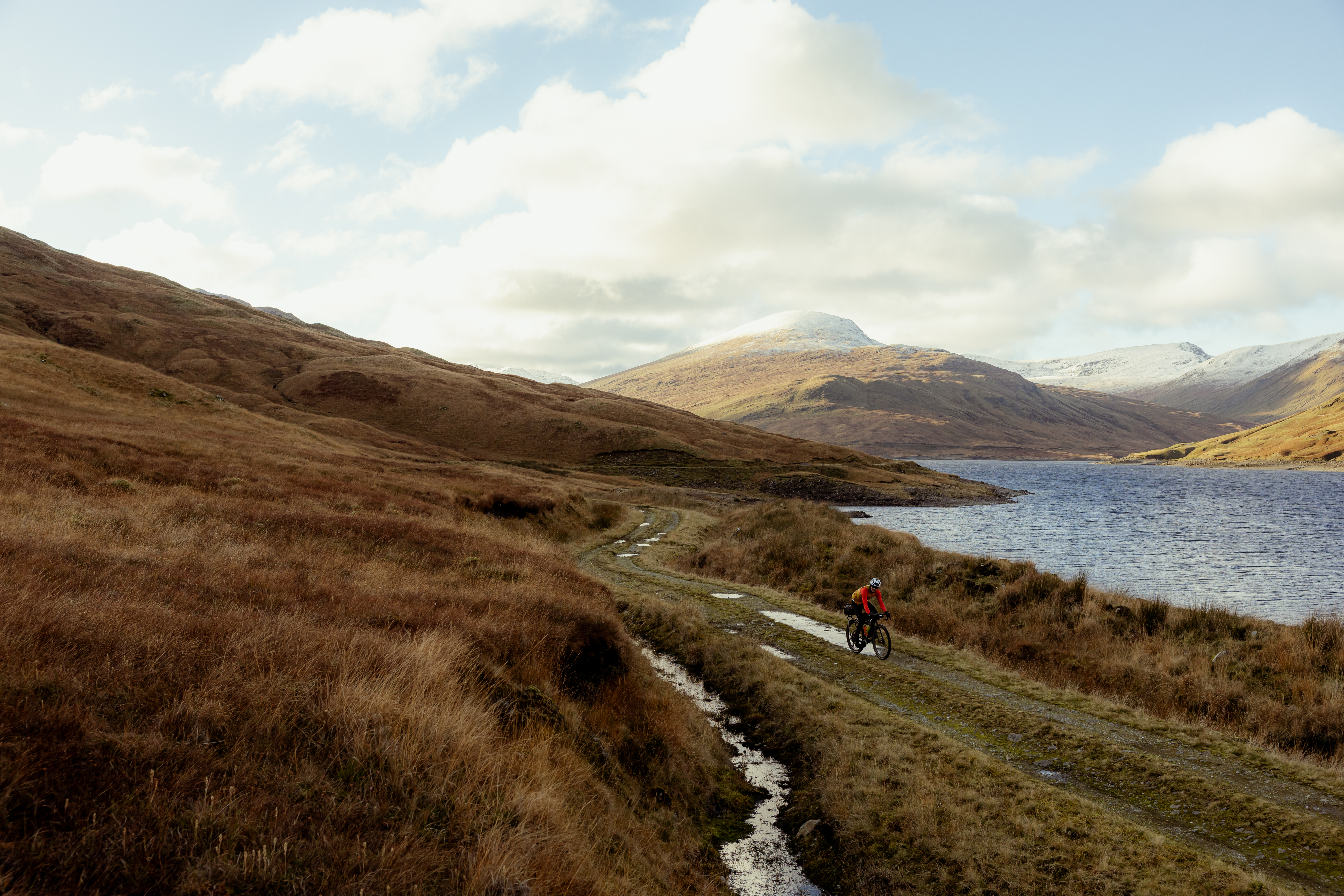 Lone rider on a gravel track beside a loch below snow-dusted hills