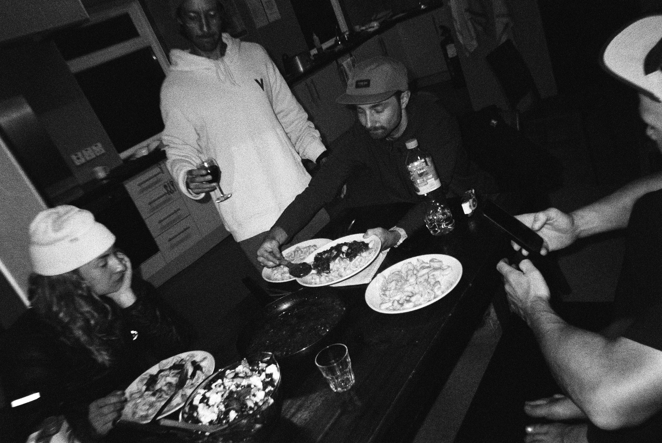 People serving plates of food at a crowded table indoors at night