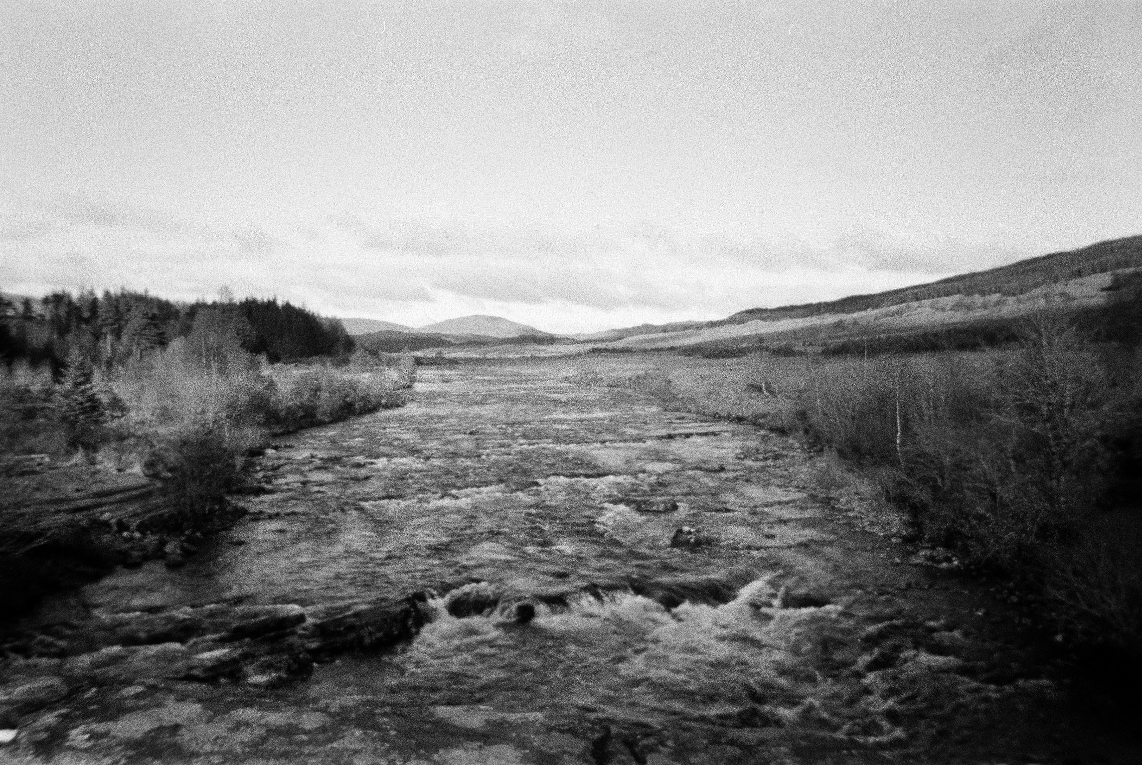 Wide braided river running through open moorland, black and white