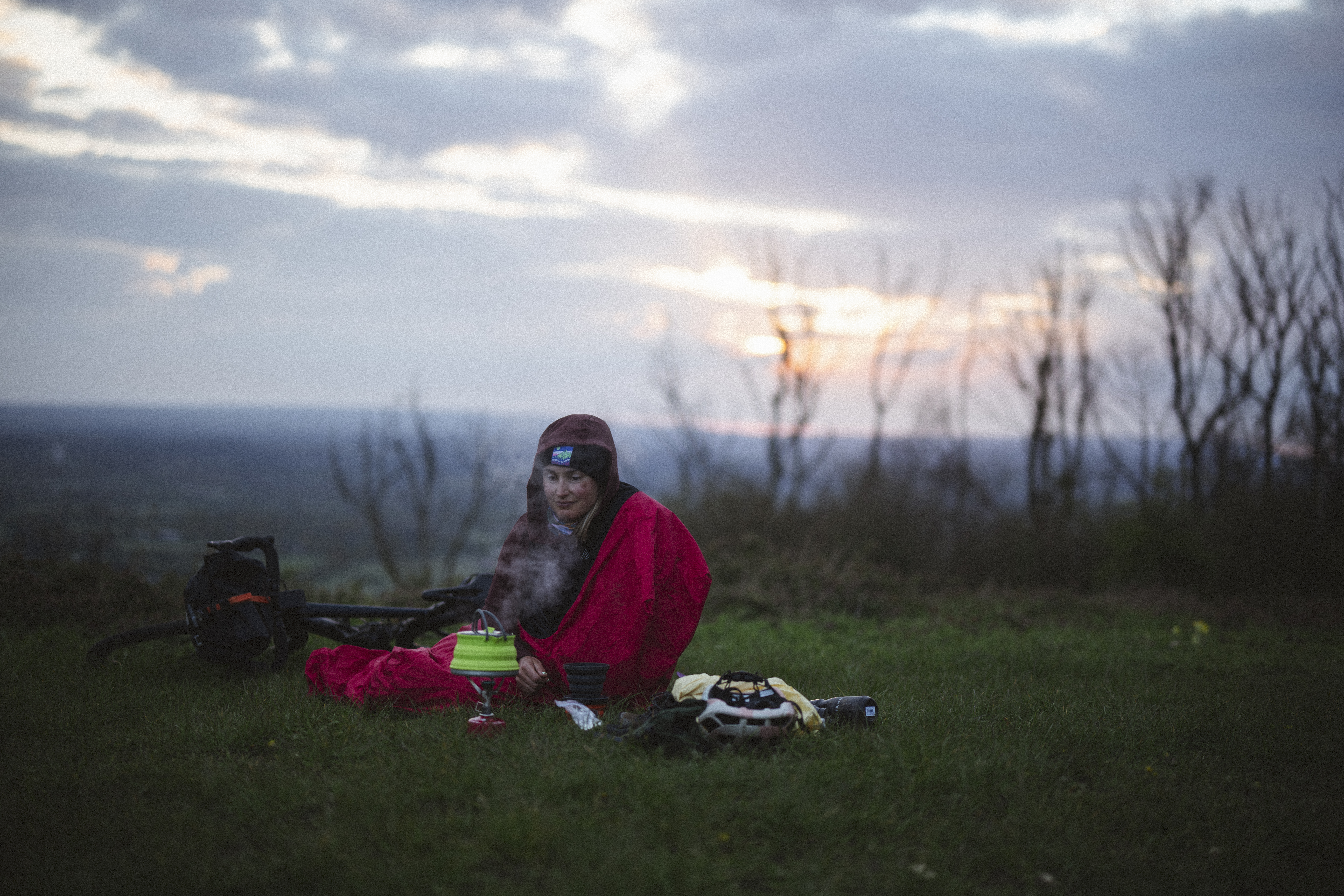 Rider wrapped in a red bivvy on a grassy hilltop at sunrise