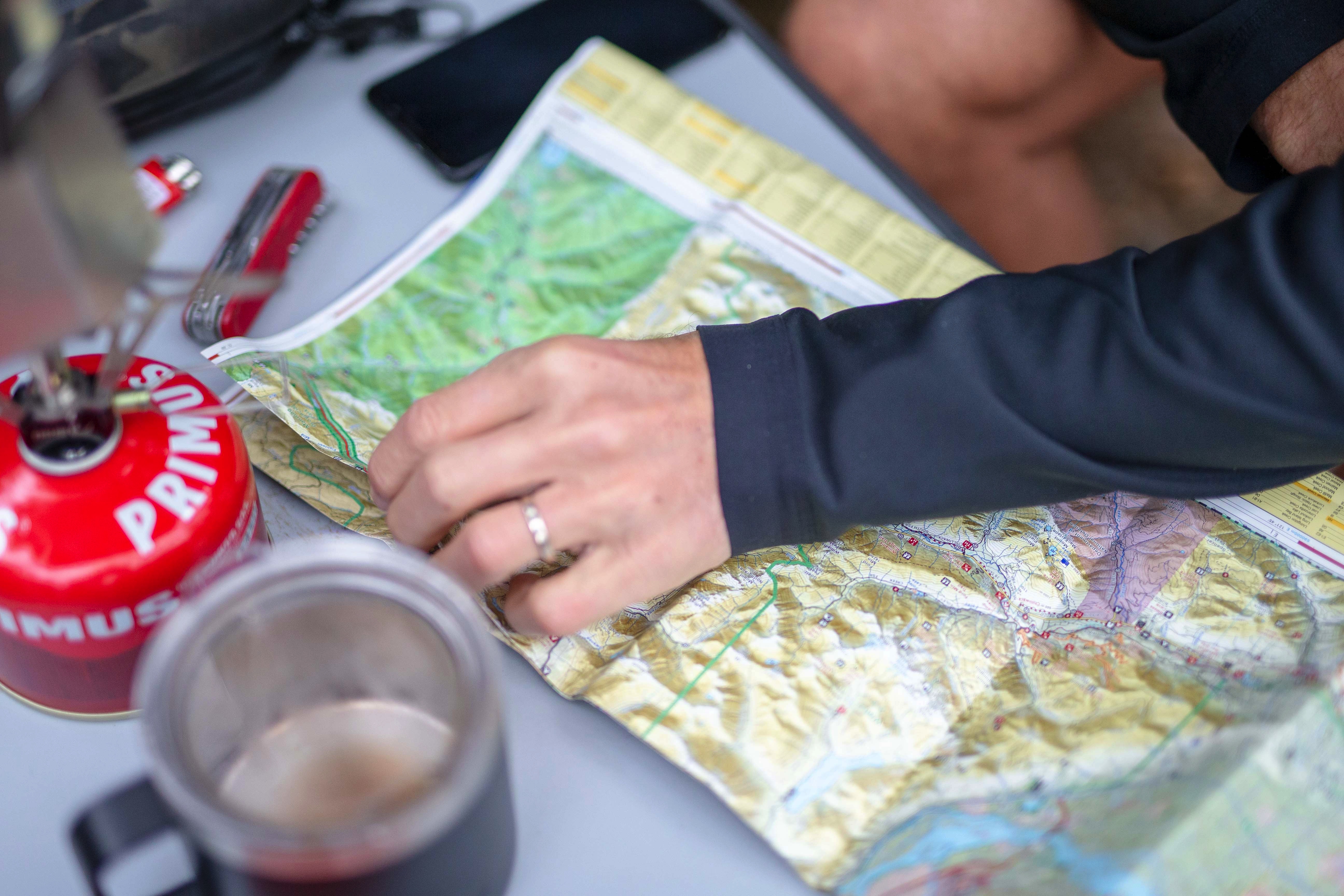 Hands on a paper map beside a stove and a mug of coffee