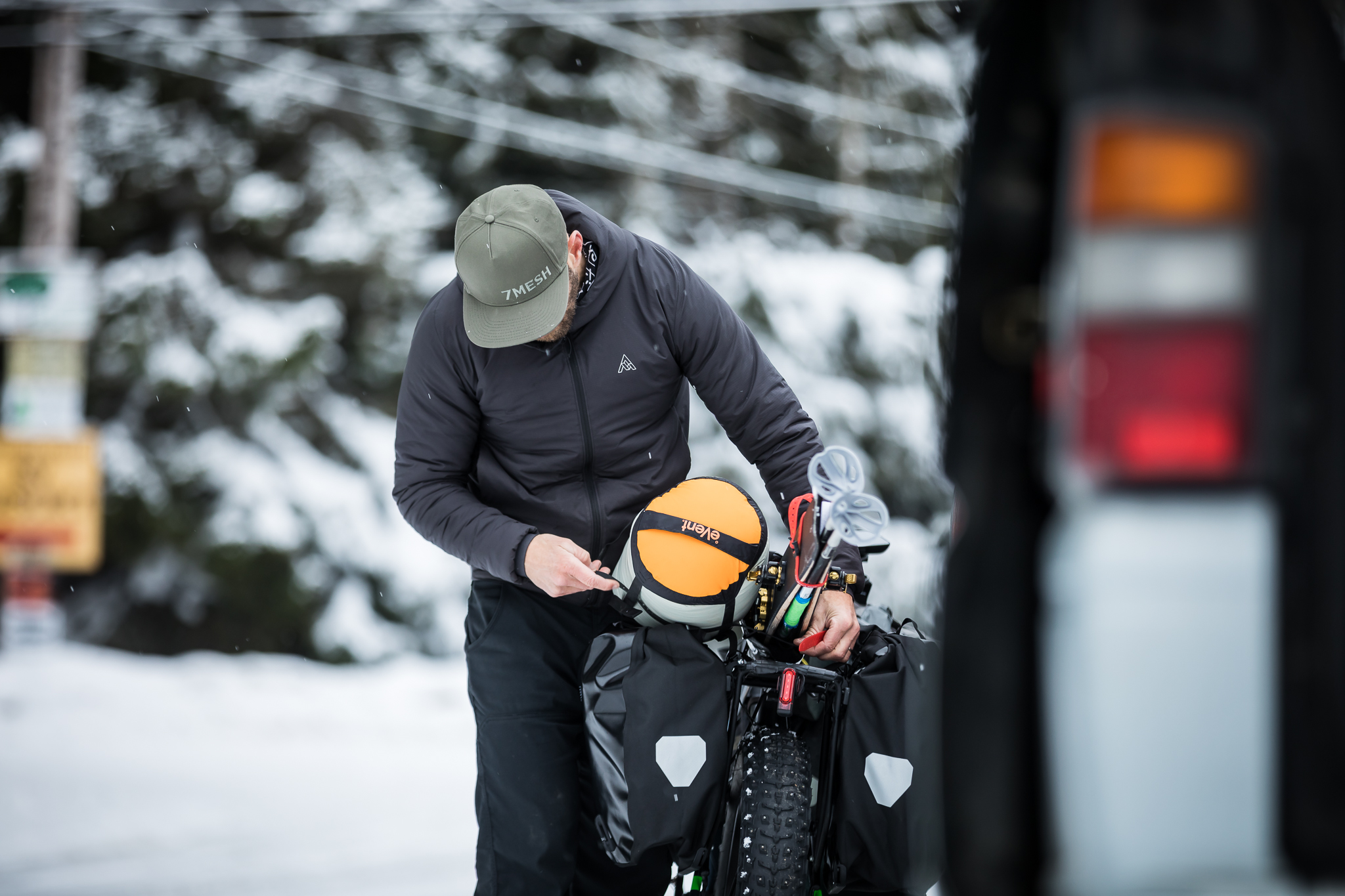 Rider loading a fat bike beside a vehicle in falling snow