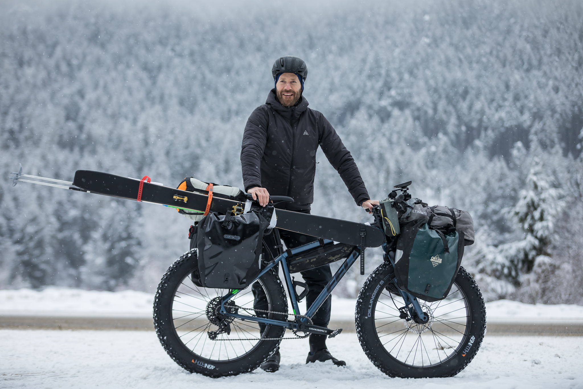 Rider with a ski-carrying fat bike on a snowy road below frosted forest