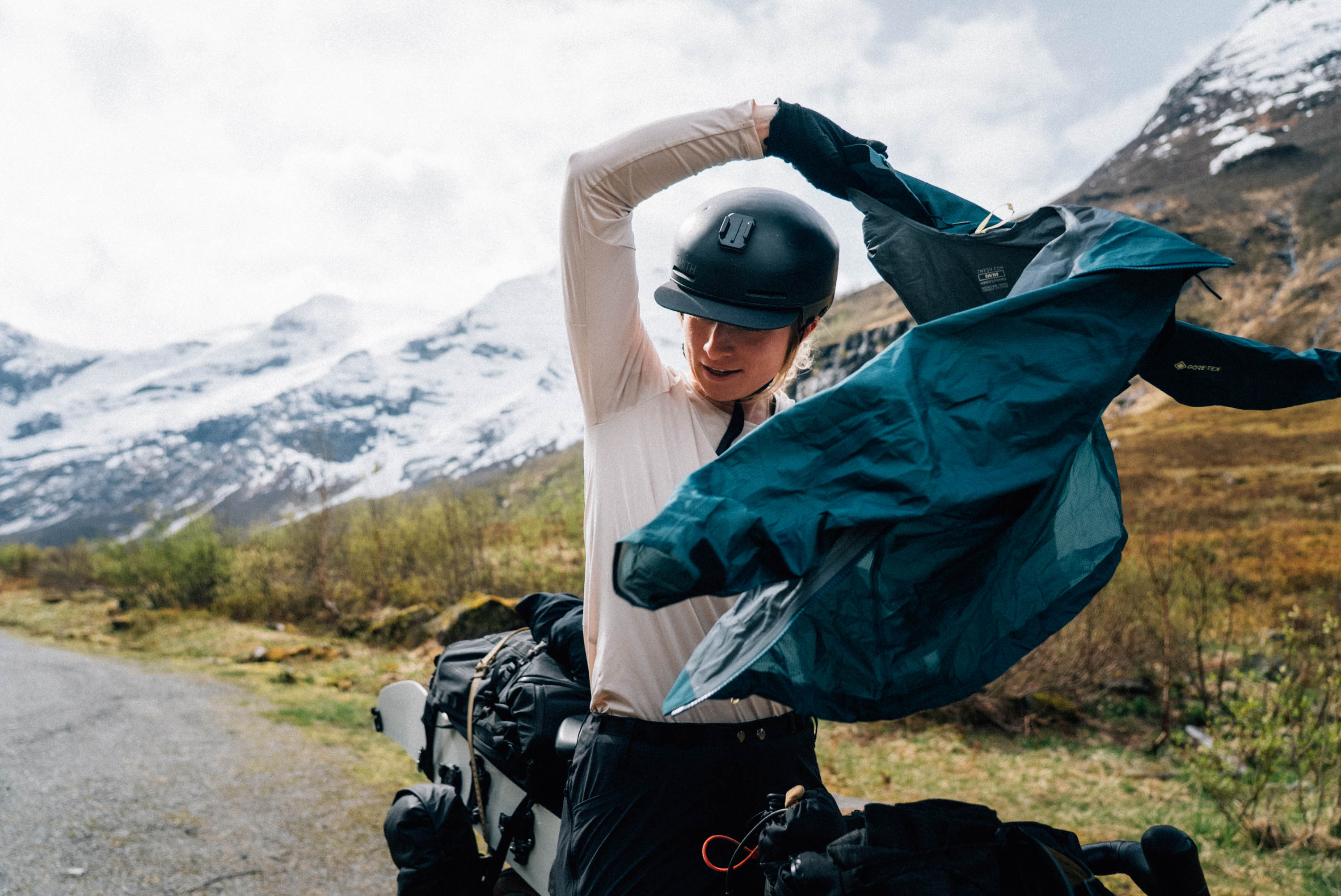 Rider pulling on a green waterproof jacket beside a loaded bike
