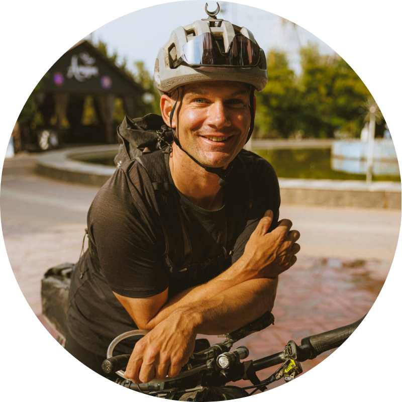Portrait of Alex Kopp smiling in a helmet beside a loaded bike