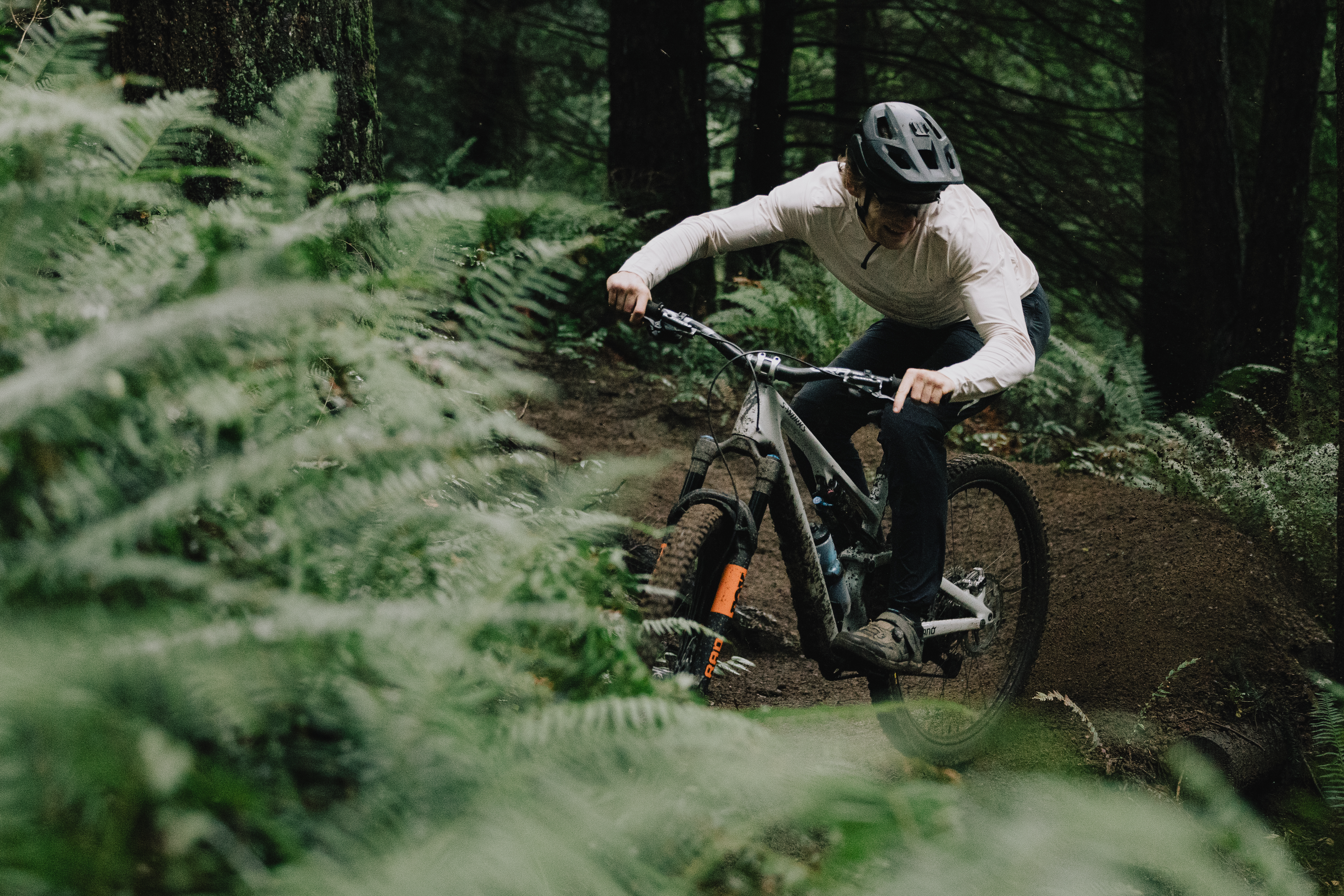 Elliot Jamieson cornering on a dirt trail through waist-high ferns under tall conifers