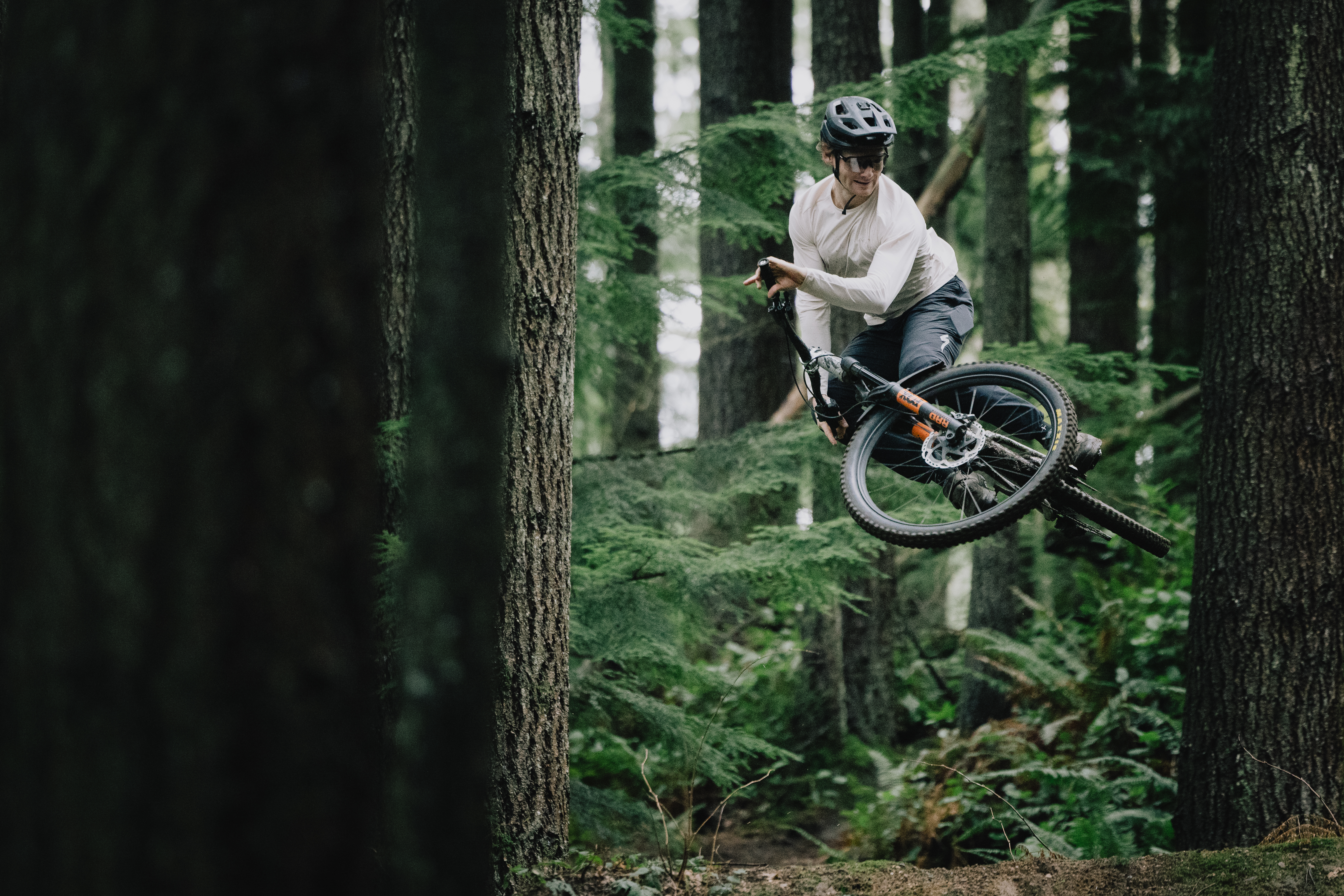 Elliot Jamieson airborne between two large tree trunks with the bike turned sideways