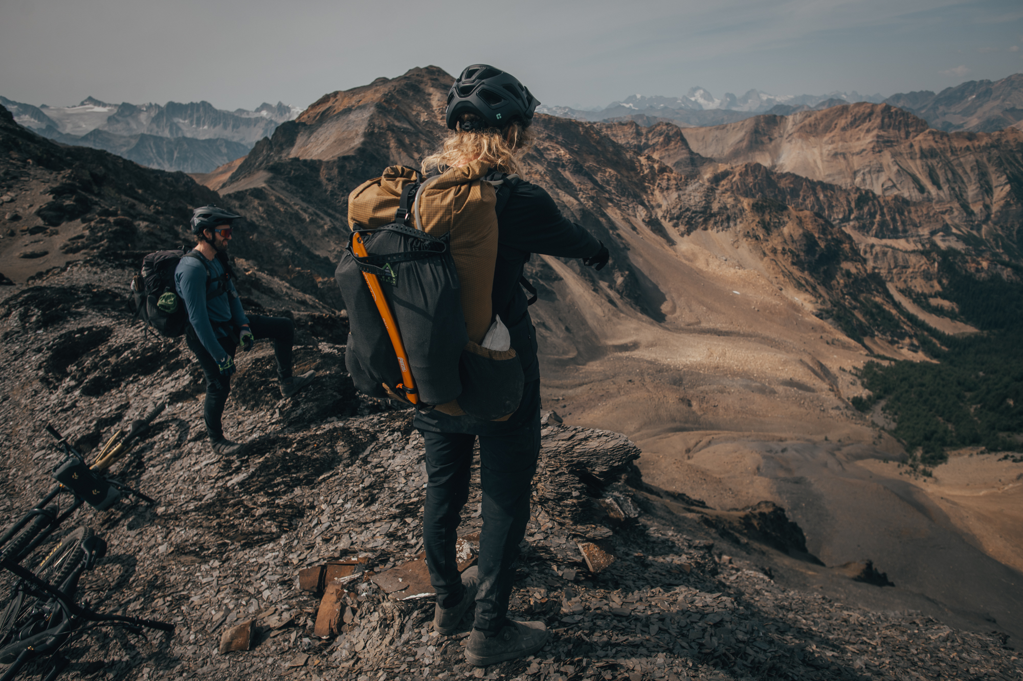 Two riders pushing loaded bikes down a dark scree slope