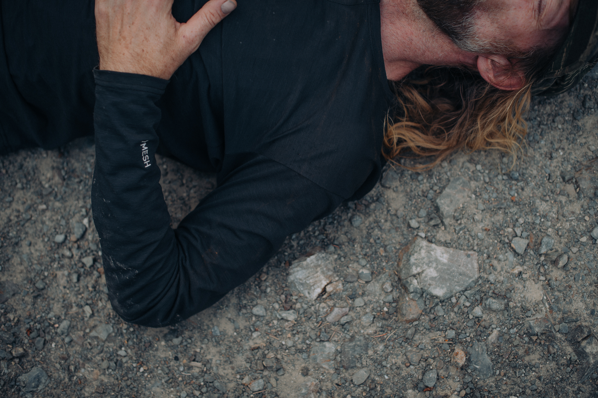 Rider lying face down on gravel beside the road, spent