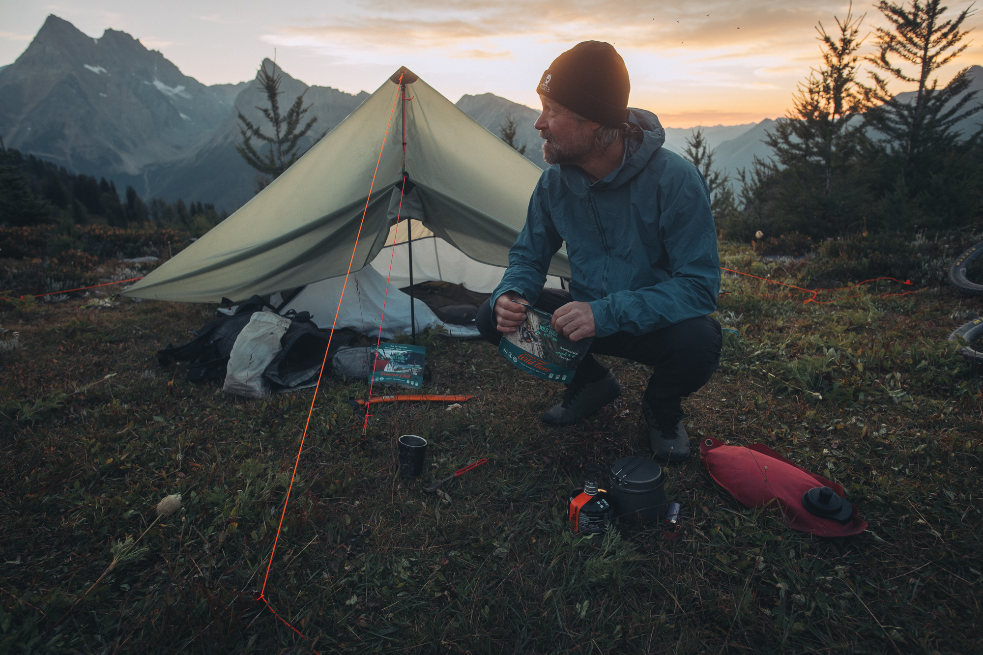 Rider crouched by a pyramid tent and stove at an alpine camp