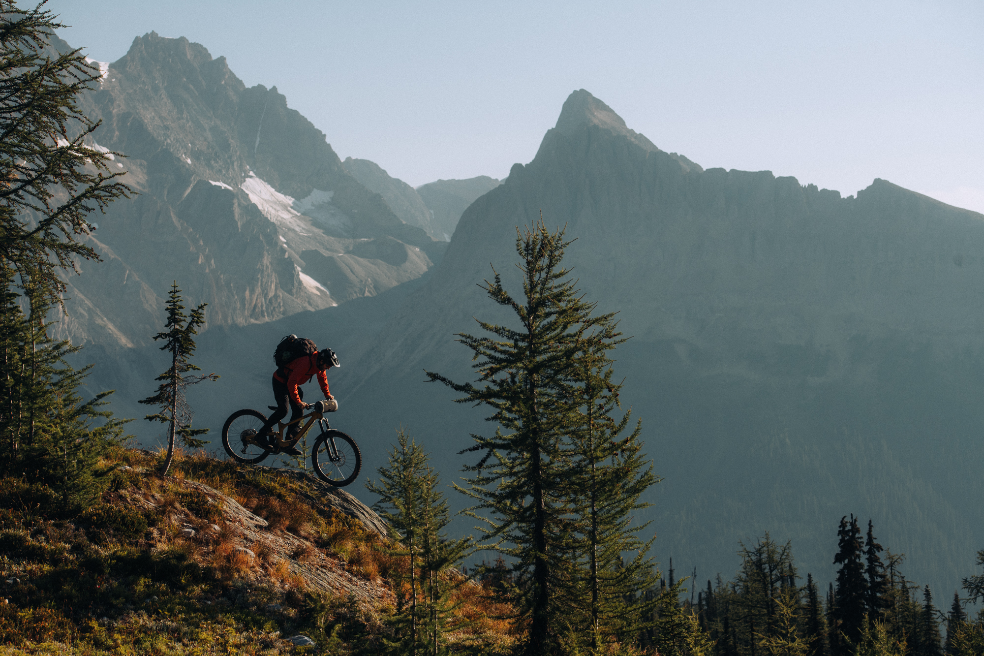 Rider descending a rocky slope below a sharp glaciated peak