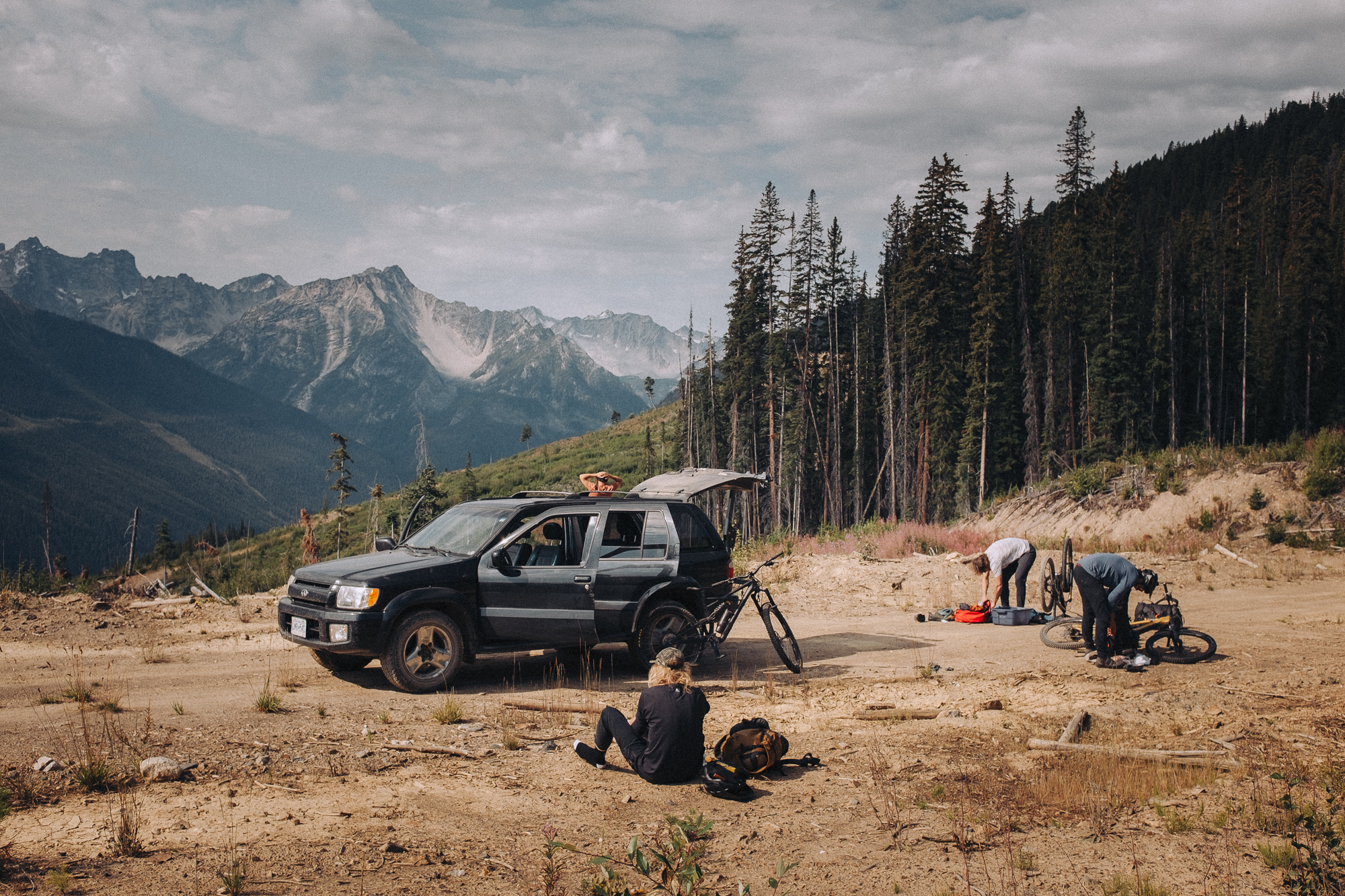 Crew packing bikes beside a truck at a dusty trailhead in the mountains