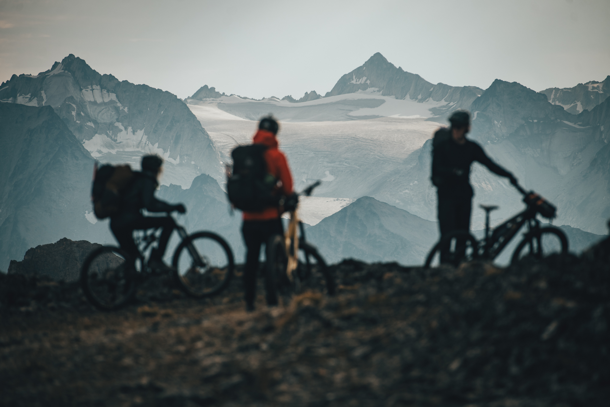 Three riders with loaded bikes looking out at a glaciated mountain range