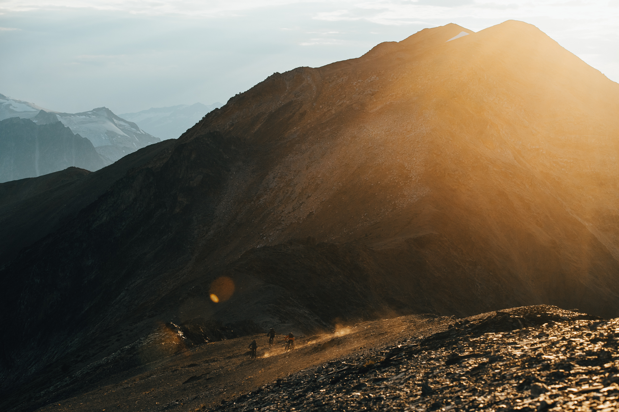 Distant riders on a sunlit ridge below a large pyramid peak