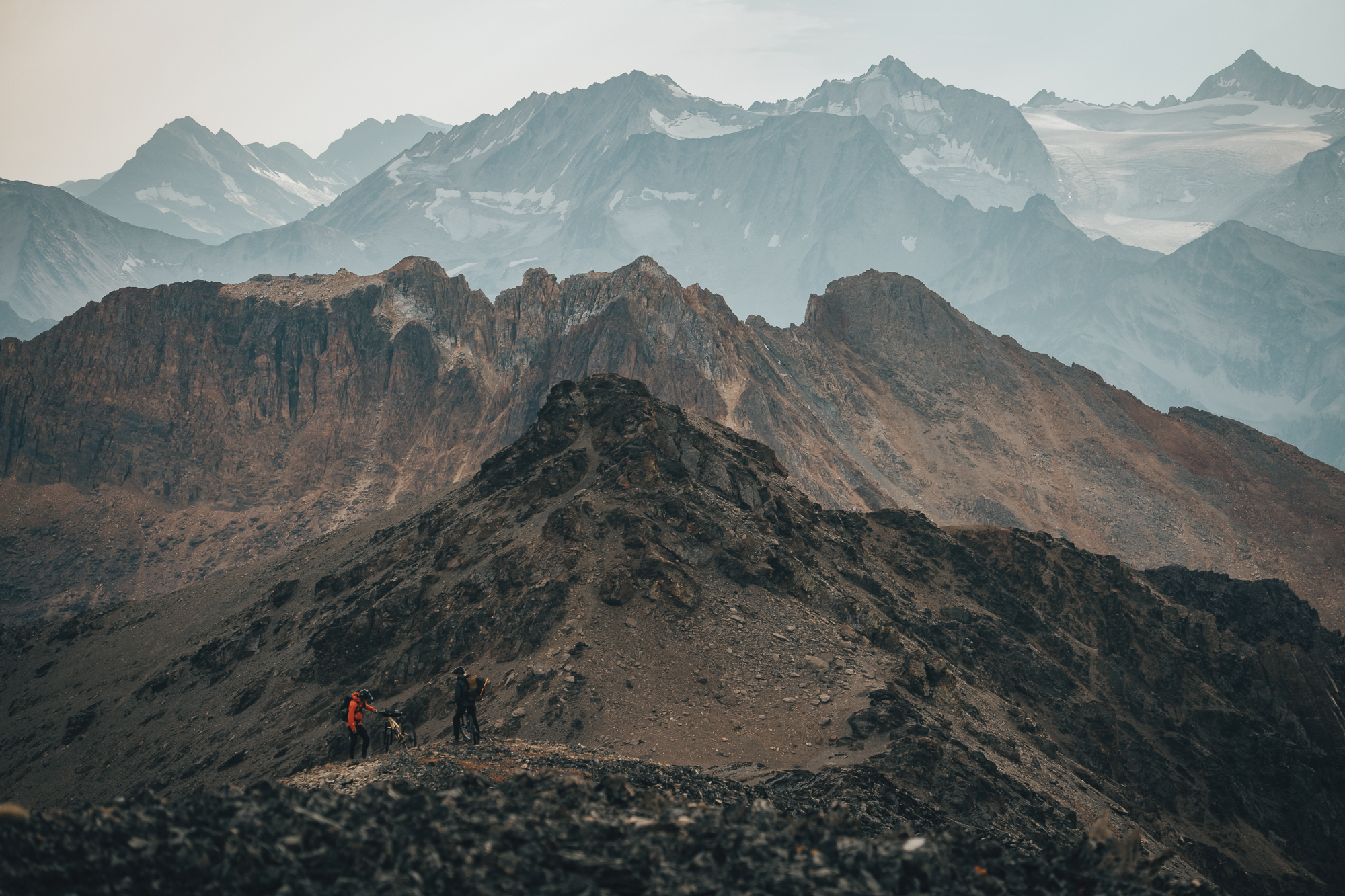 Two tiny figures on a scree ridge below a wall of glaciated peaks