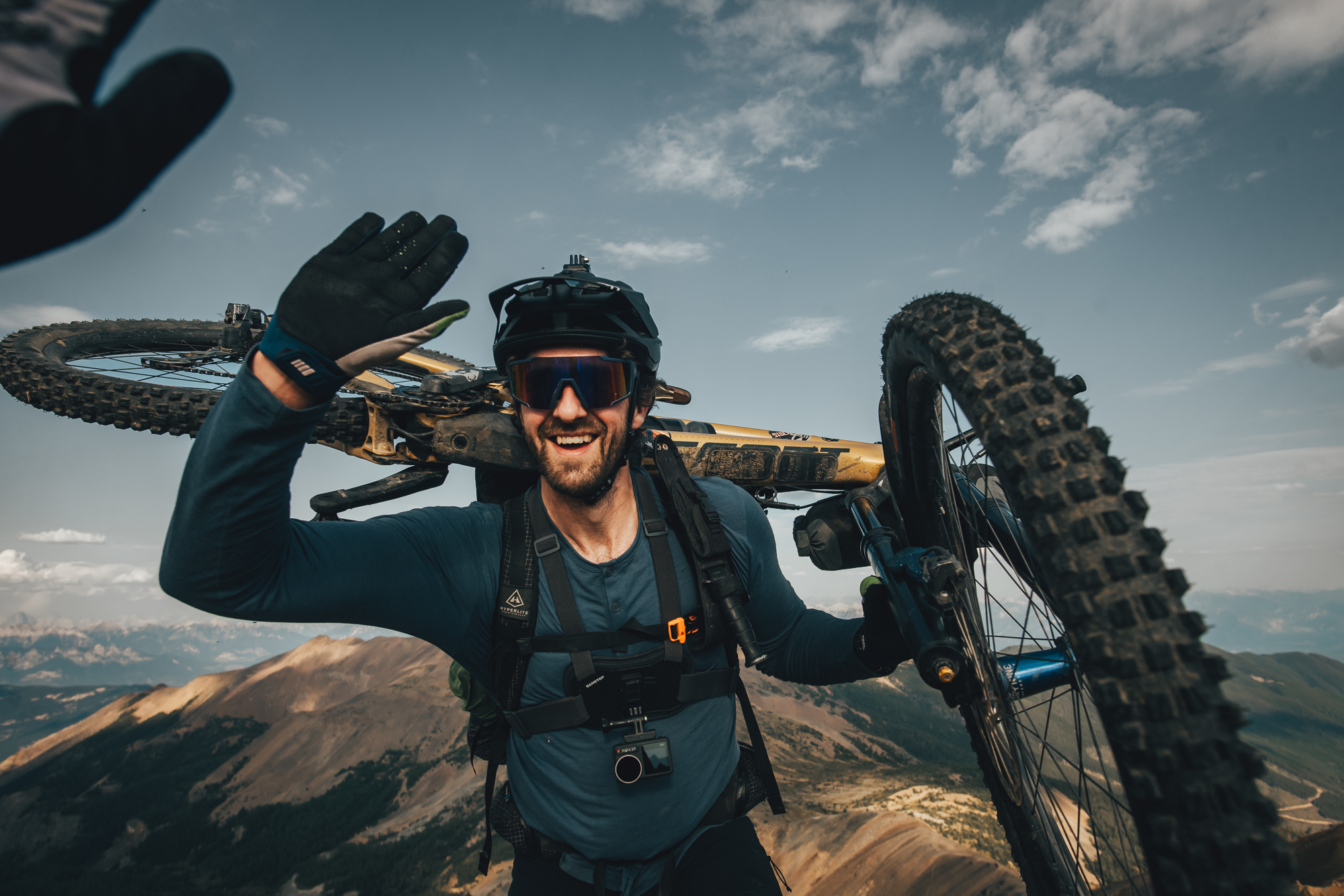 Rider grinning with a mountain bike shouldered on a high ridge