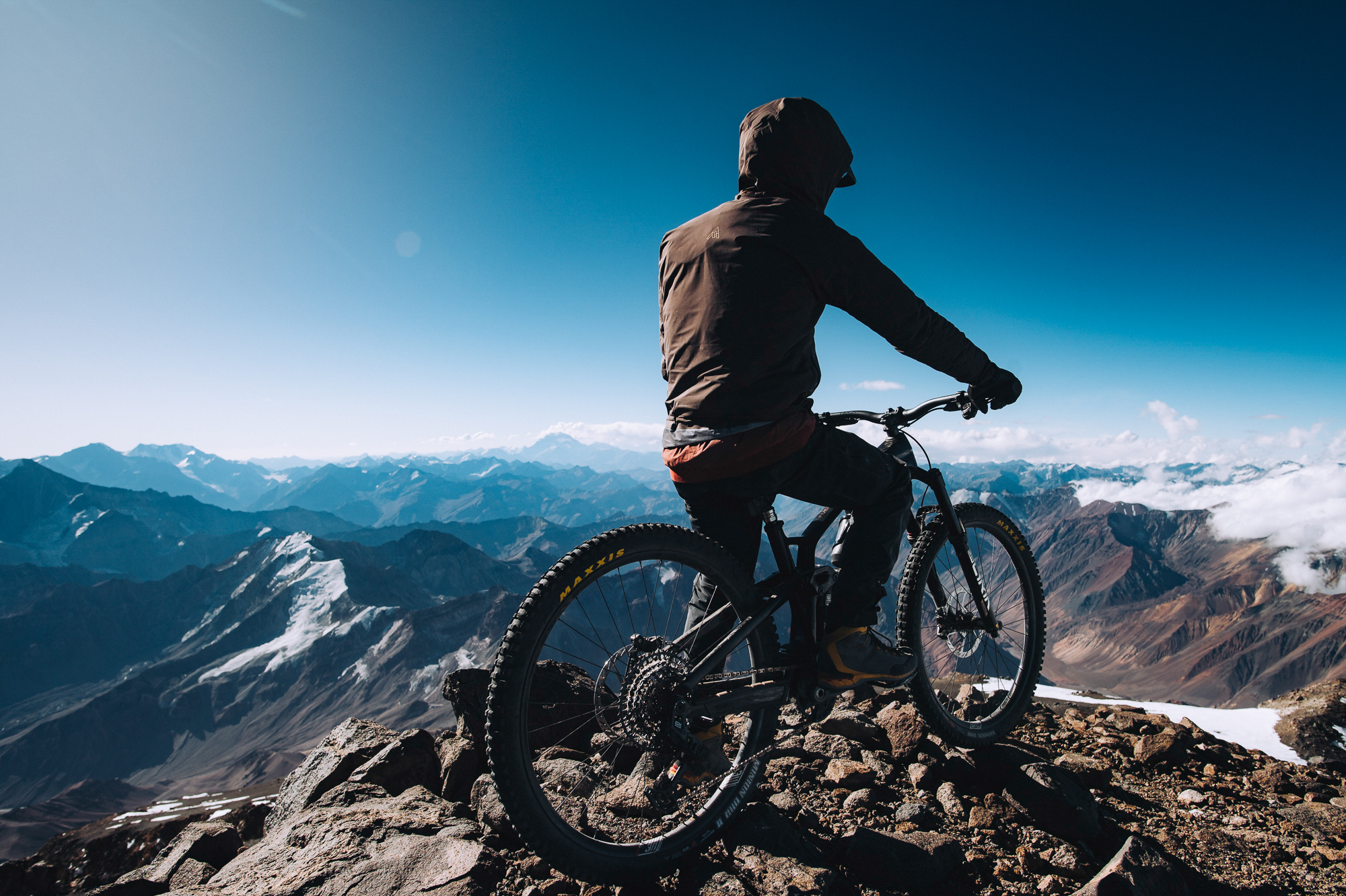Rider on a bike on a summit ridge above a sea of distant blue peaks