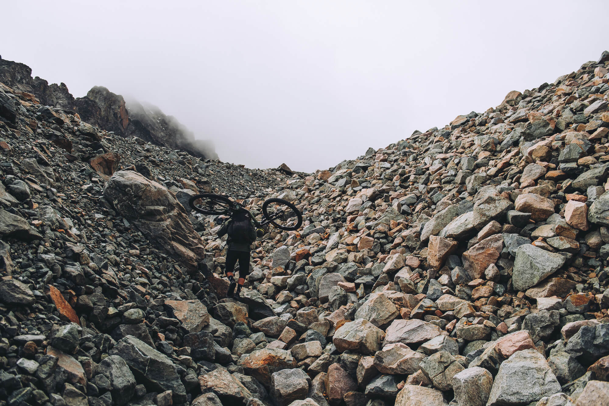 Rider carrying a bike up a boulder field into fog