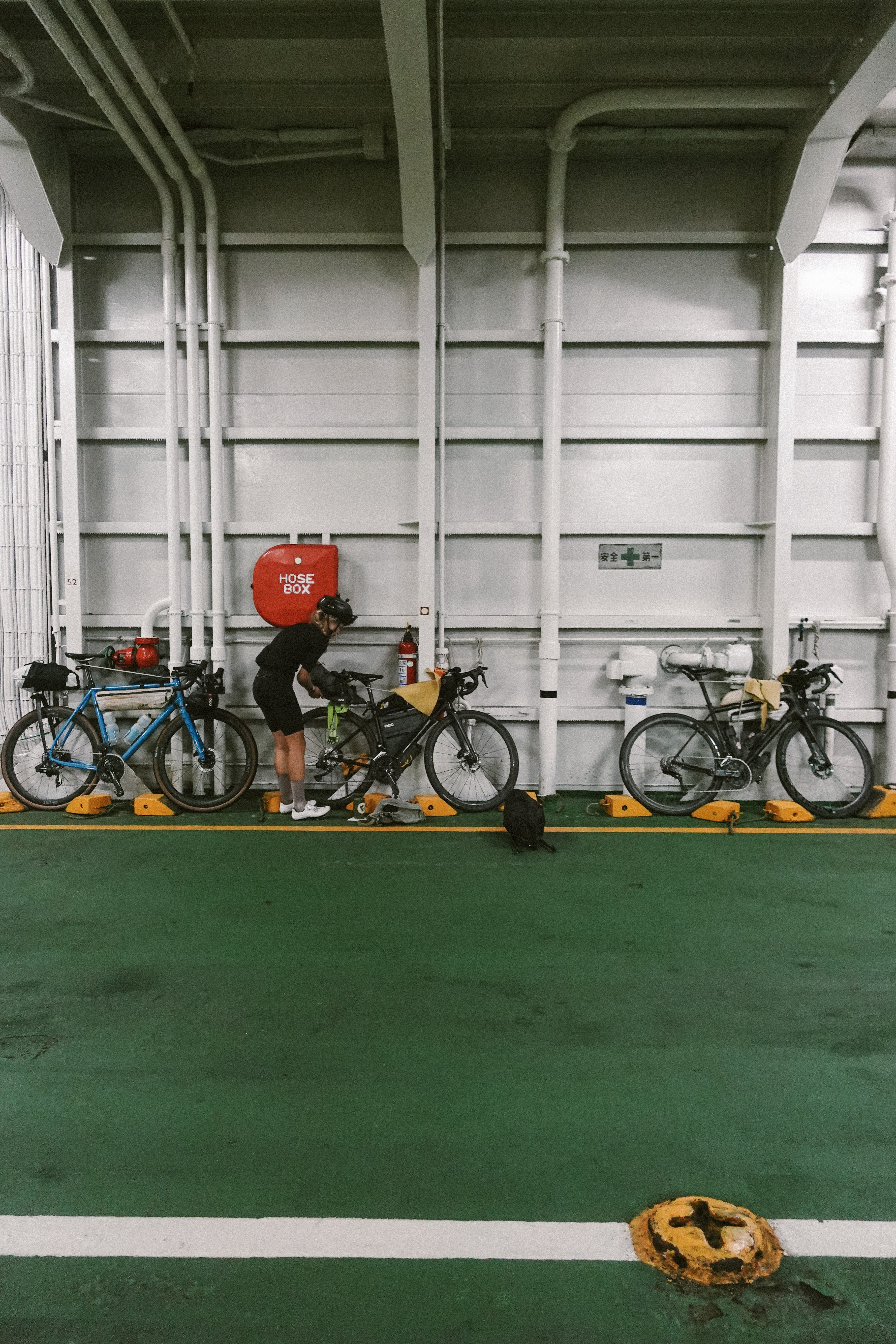 Rider packing bags beside three loaded bikes chocked on a ferry car deck