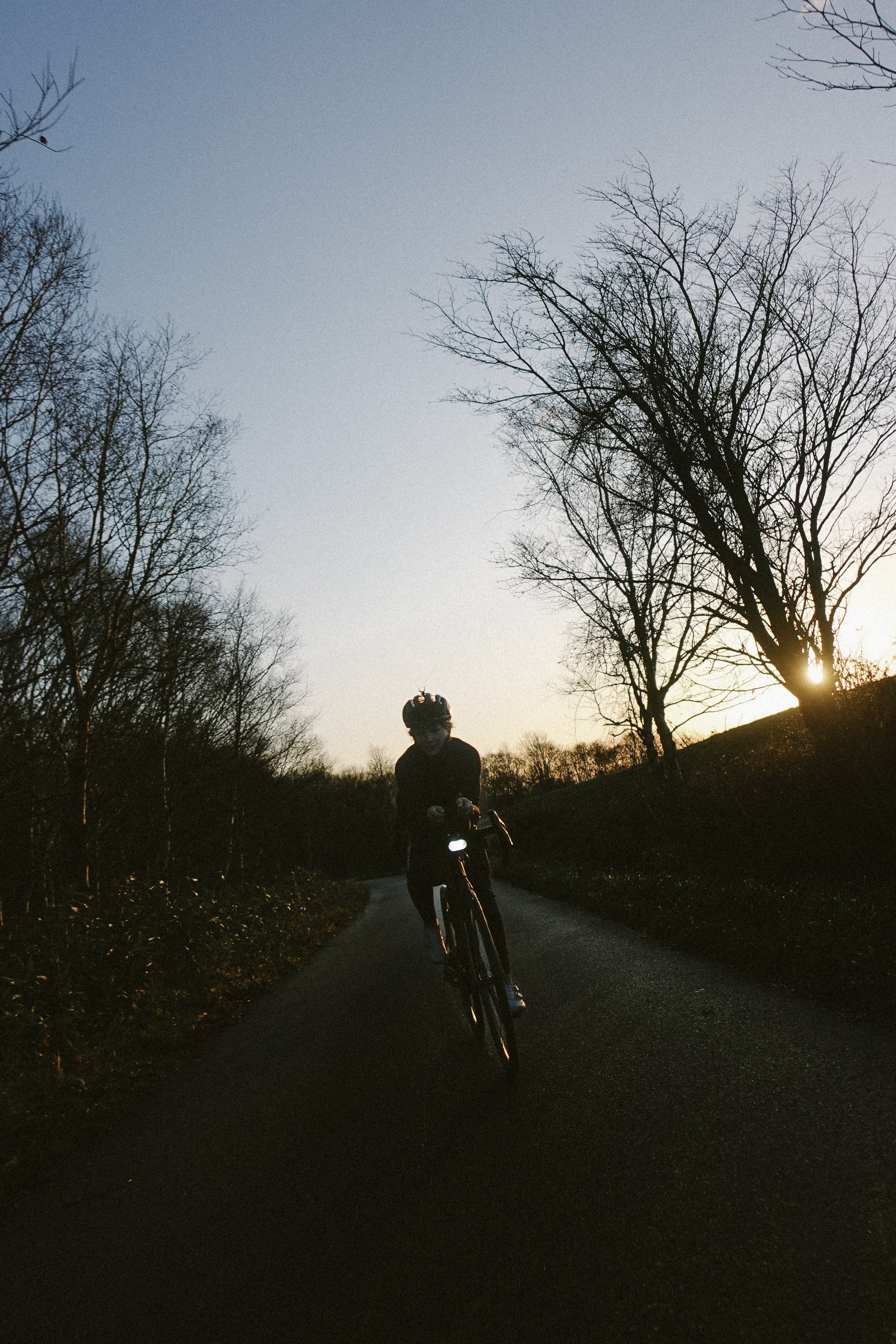 Rider with a front light on a hedged lane at sunset
