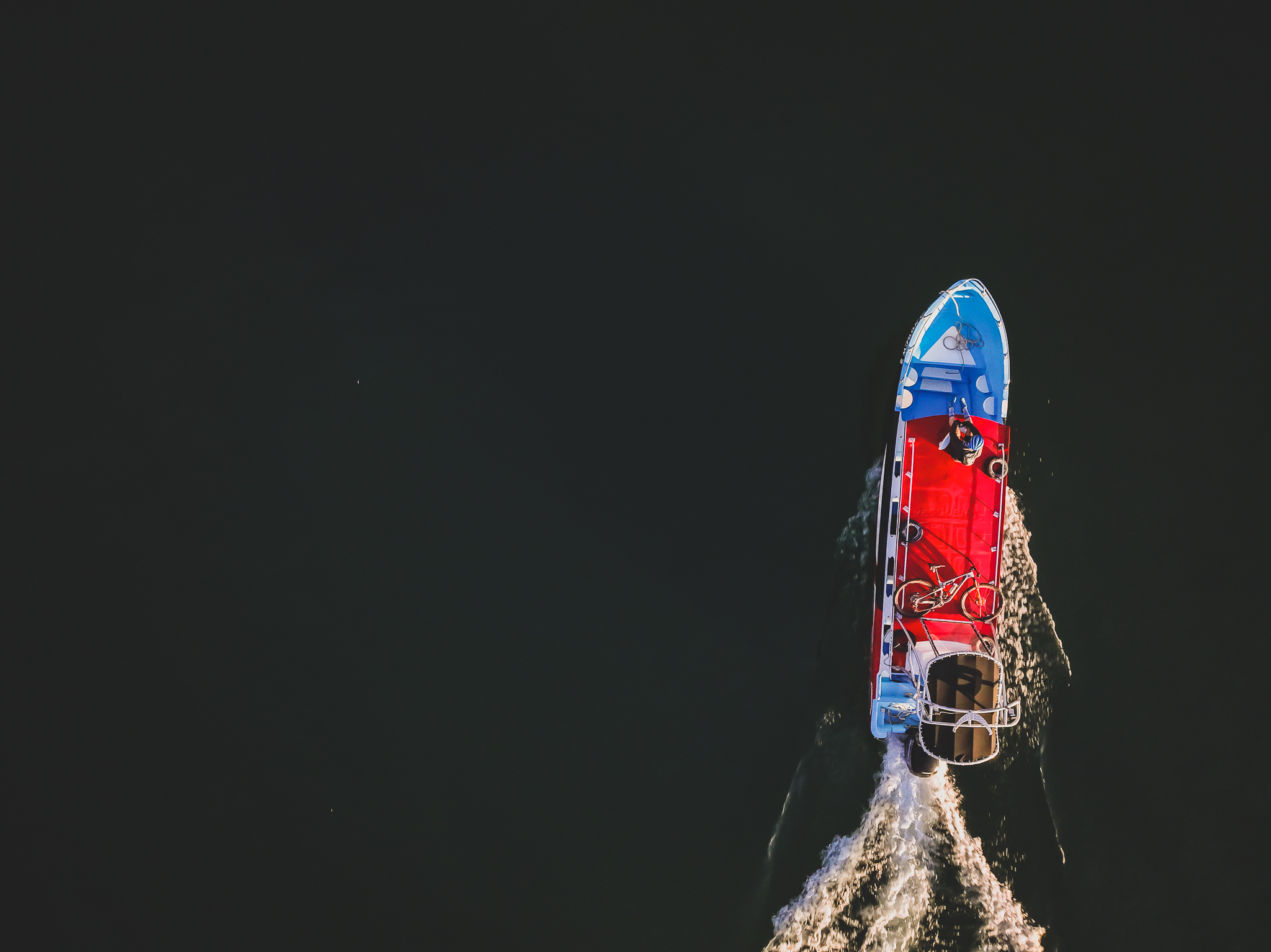 Aerial view of a small passenger boat carrying bikes across dark water