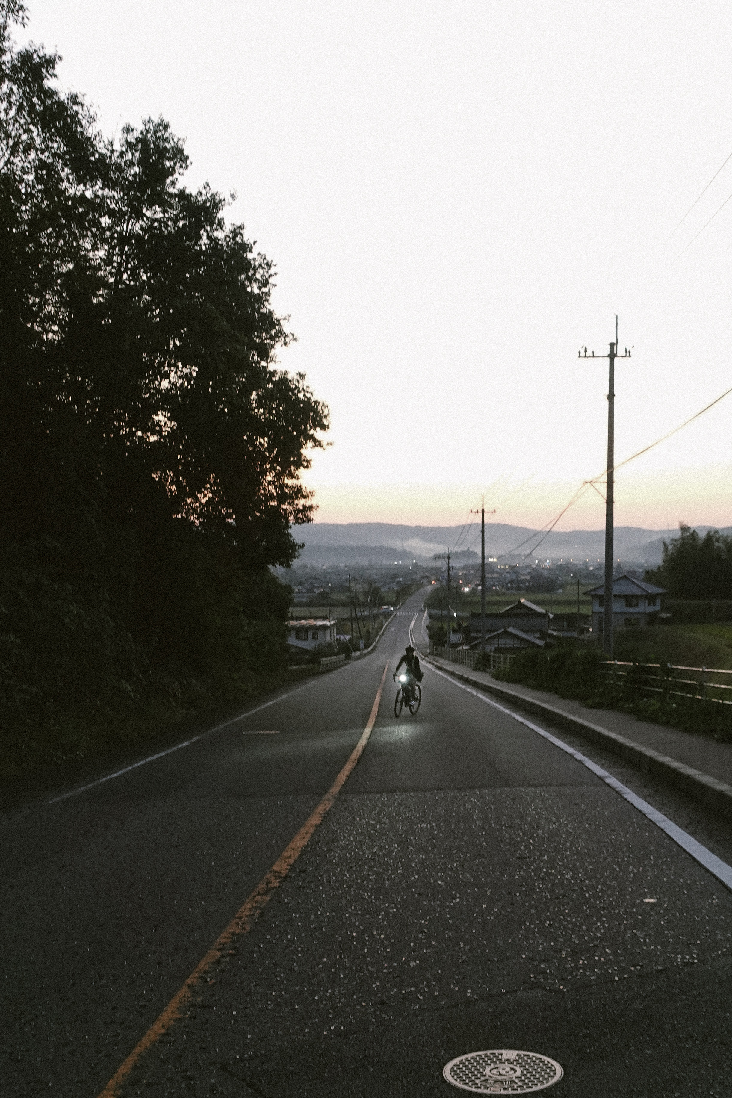 Rider descending a road toward a town at dusk with a front light on