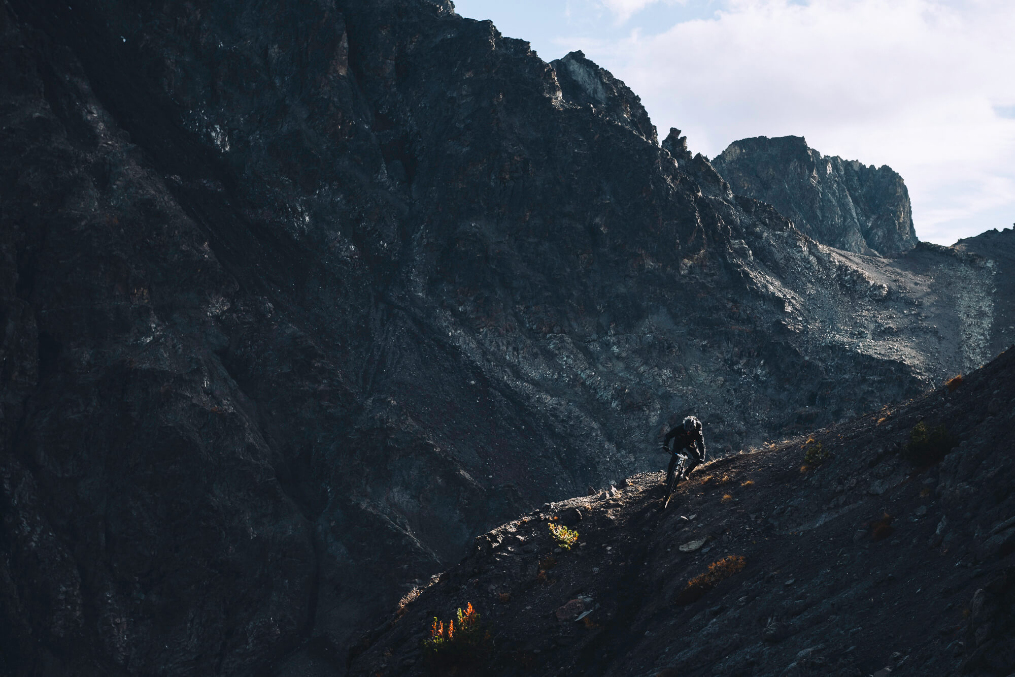 Rider descending a dark, steep slope below a large rock wall