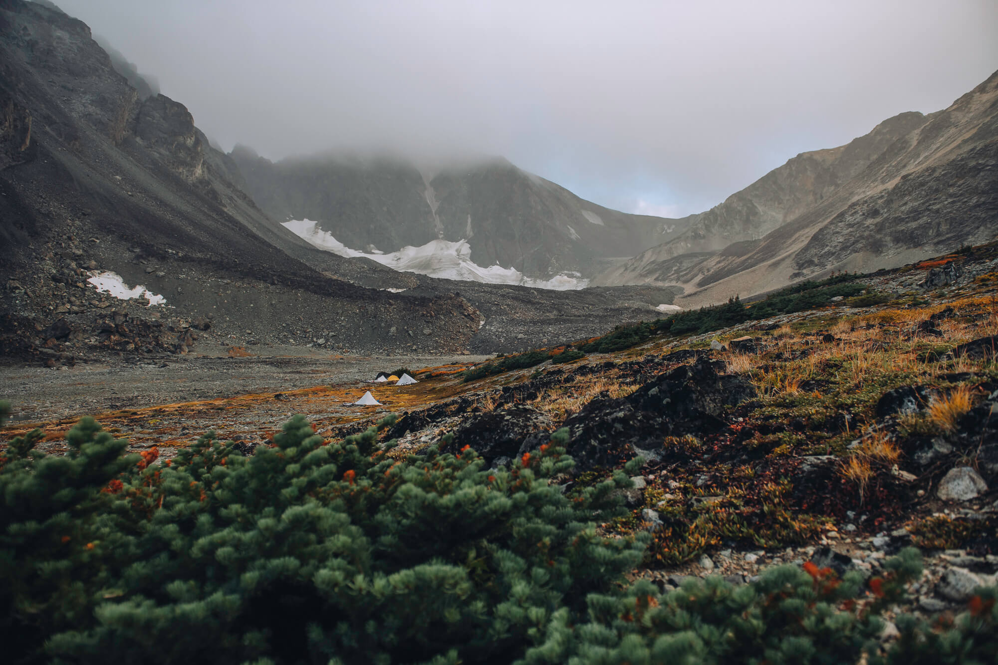 Two small tents pitched on tundra below a glacier and low cloud