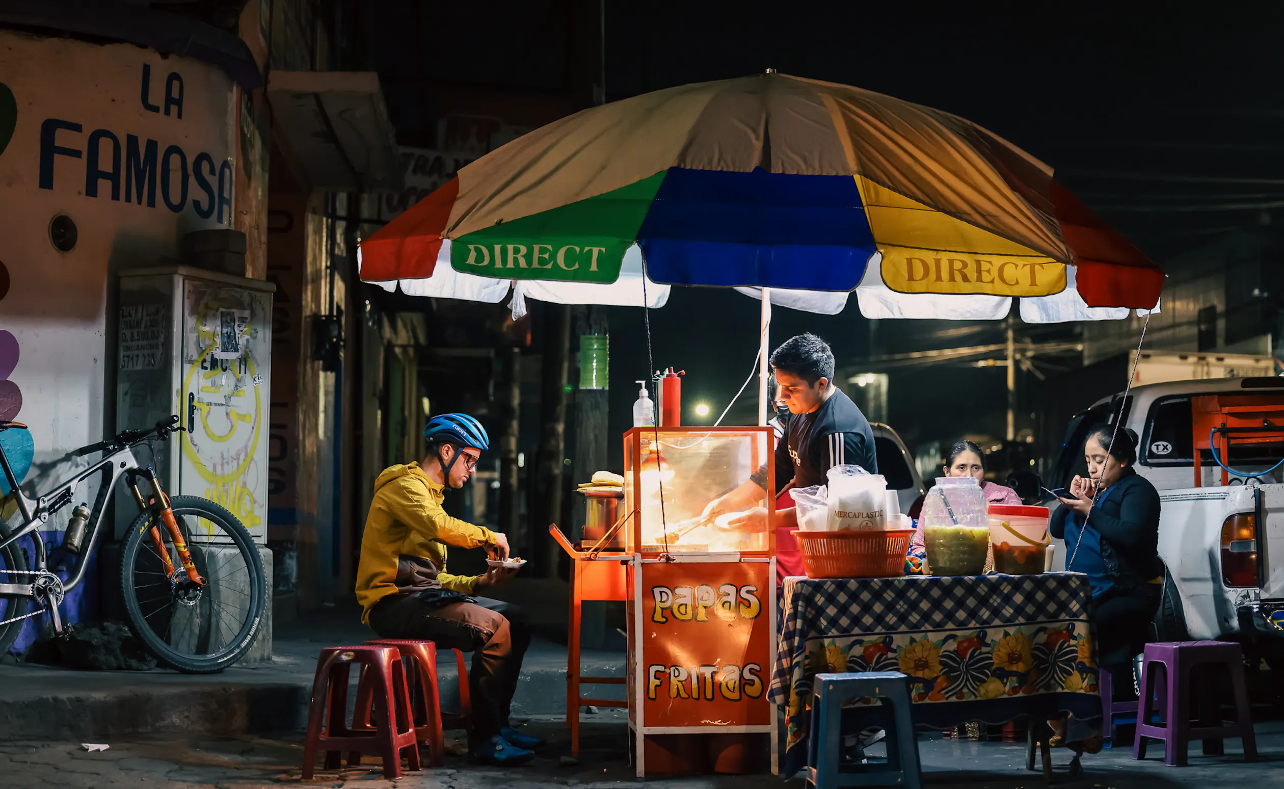 Rider eating at a lit street food stall under a striped umbrella at night