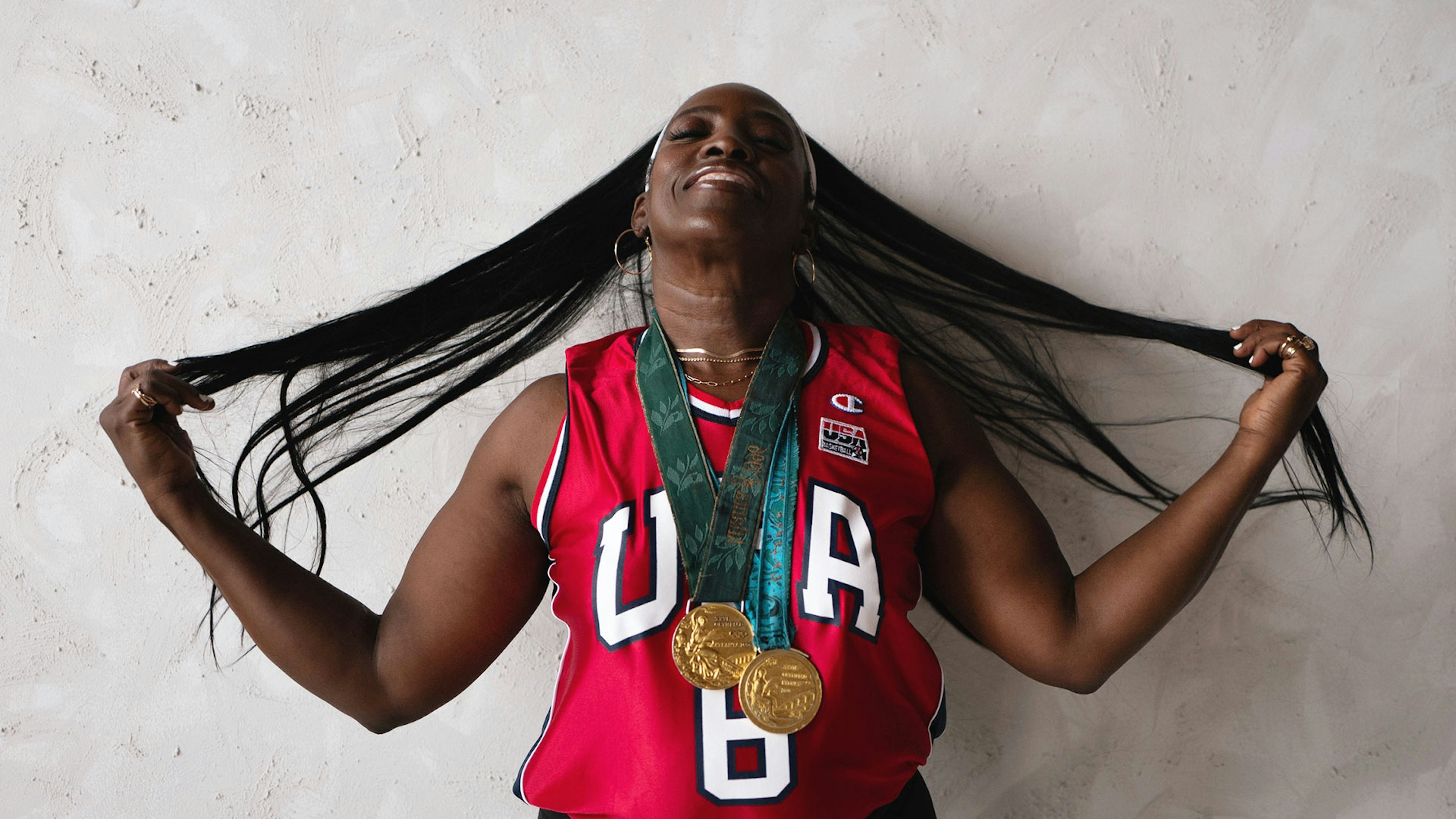 Ruthie Bolton in a USA basketball jersey, wearing Olympic gold medals and holding her long hair outstretched.
