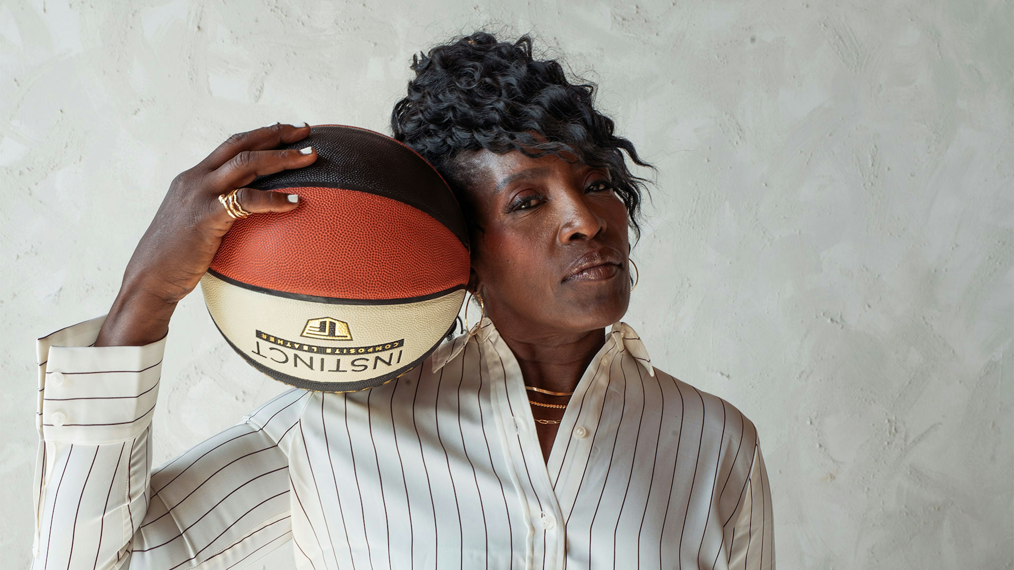 Ruthie Bolton in a white striped shirt, holding a basketball beside her face.