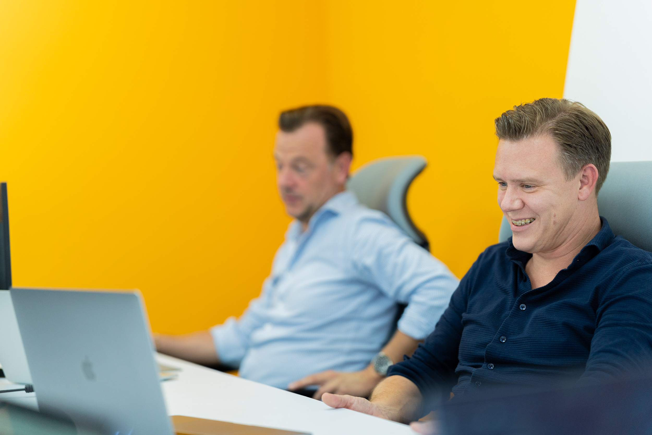 Two CC.Talent colleagues working at their desks against a bright yellow office wall