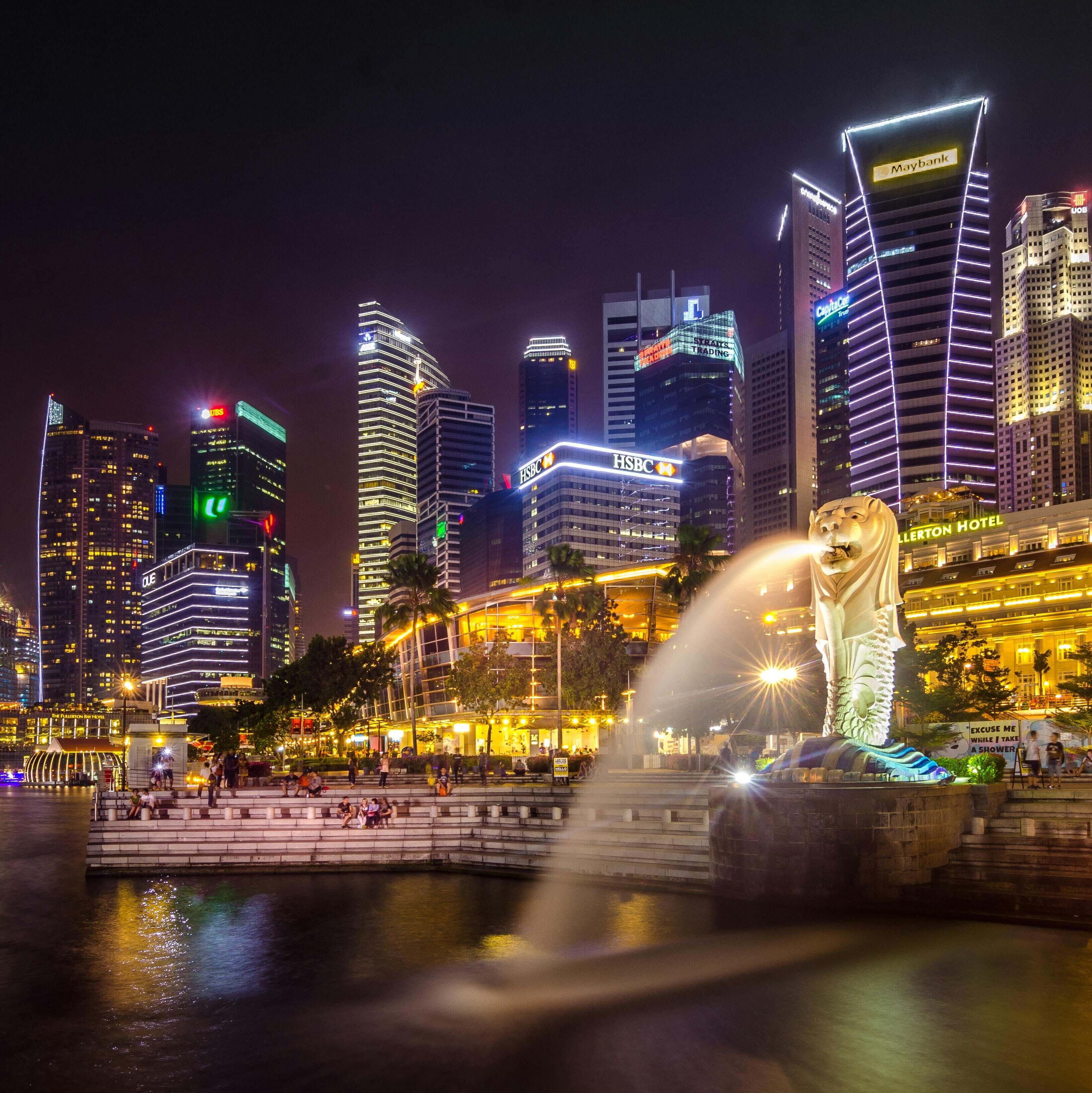 The Merlion fountain in front of Singapore's floodlit financial district skyline at night