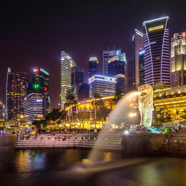 The Merlion fountain in front of Singapore's floodlit financial district skyline at night