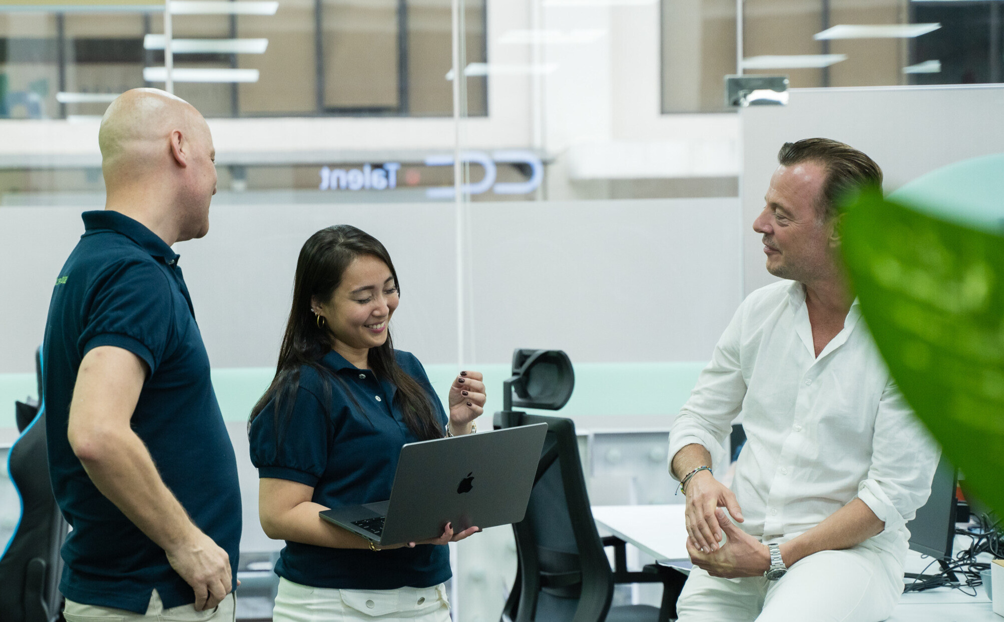 Three CC.Talent colleagues in conversation around a laptop in the office