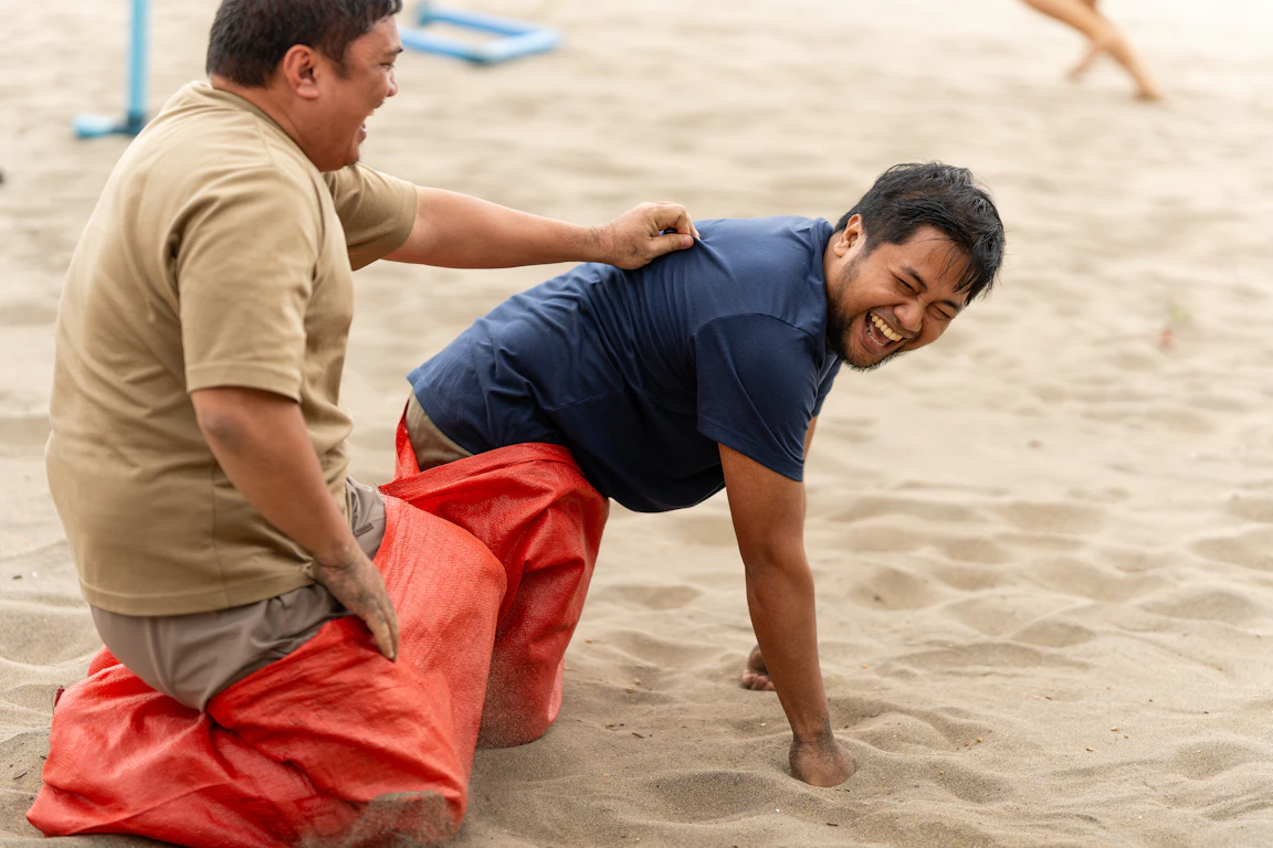 Two CC.Talent colleagues laughing together during a sack race at a team outing on the beach