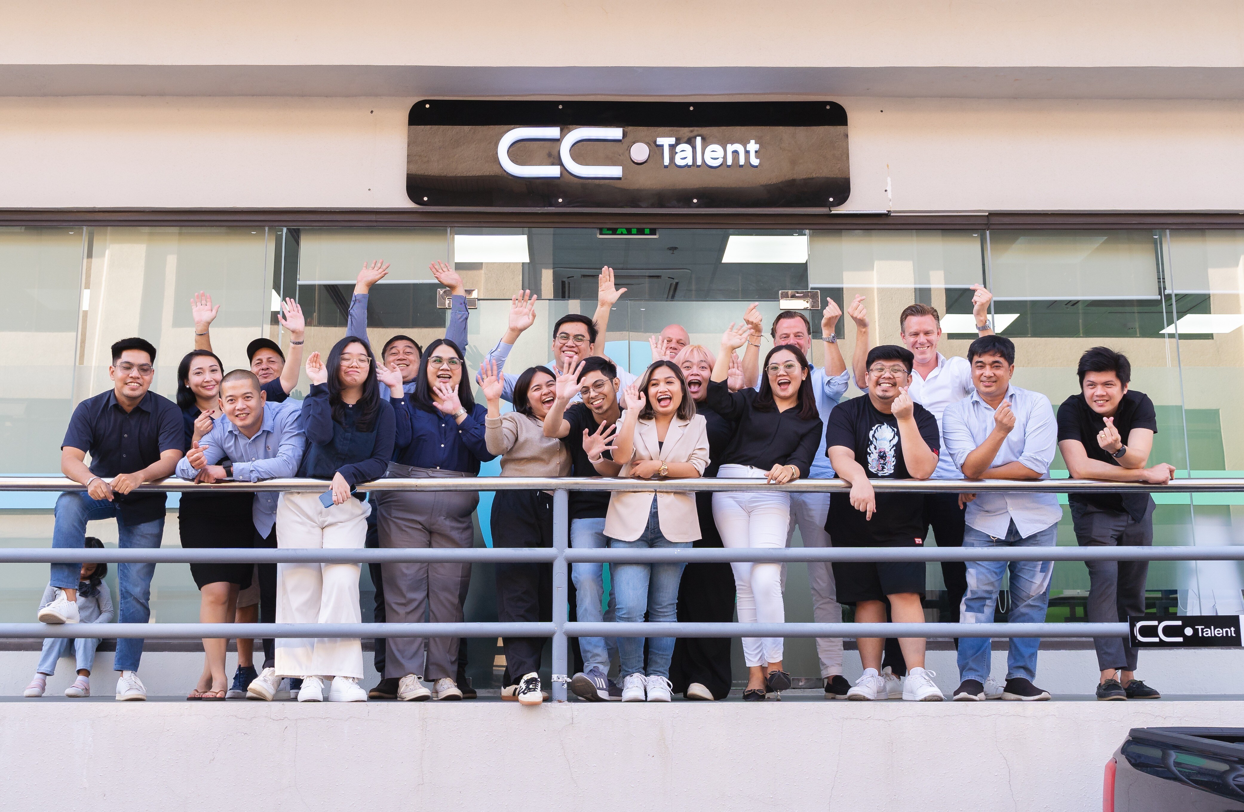 The CC.Talent team waving from the office balcony beneath the illuminated CC.Talent sign