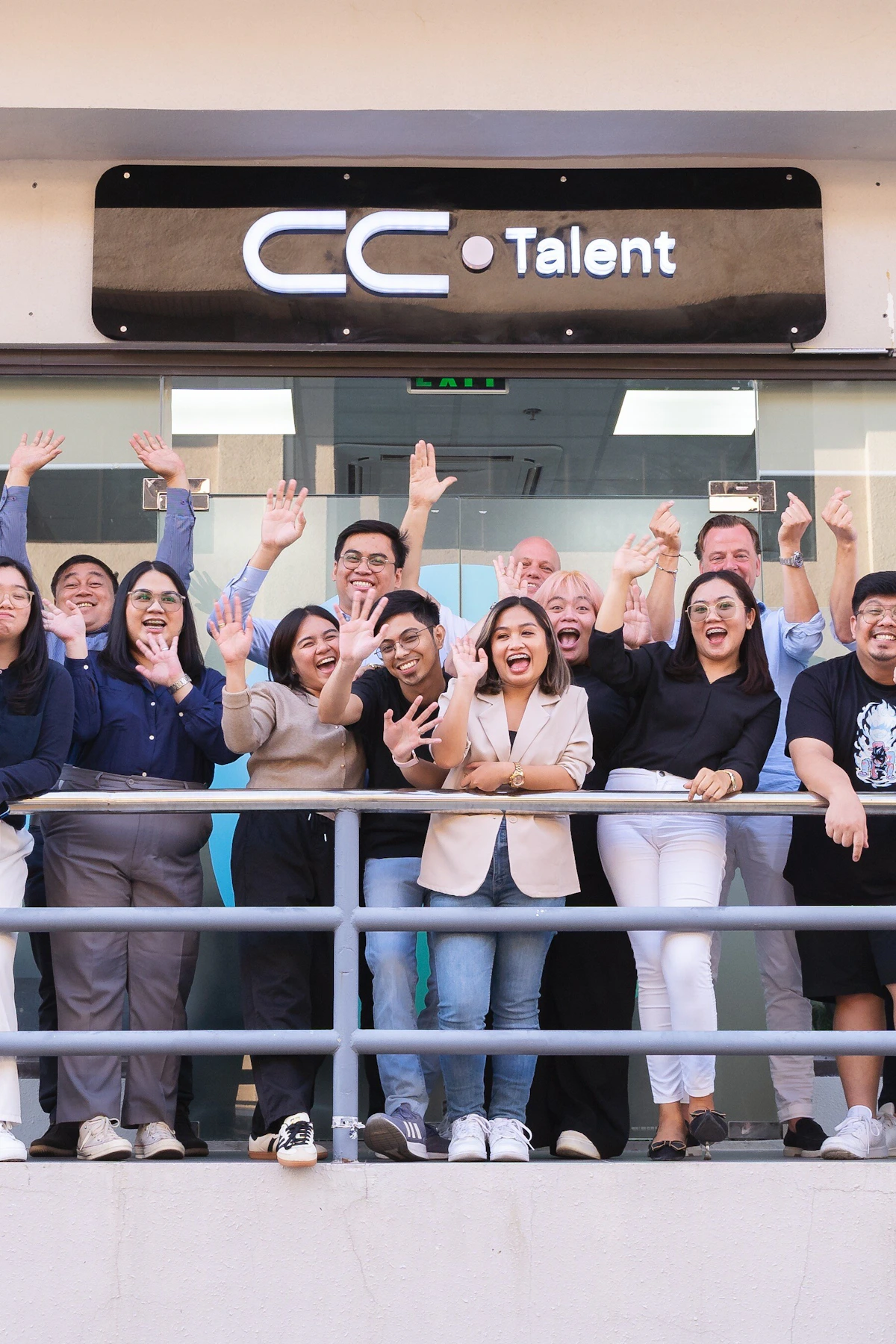 The CC.Talent team waving from the office balcony beneath the illuminated CC.Talent sign