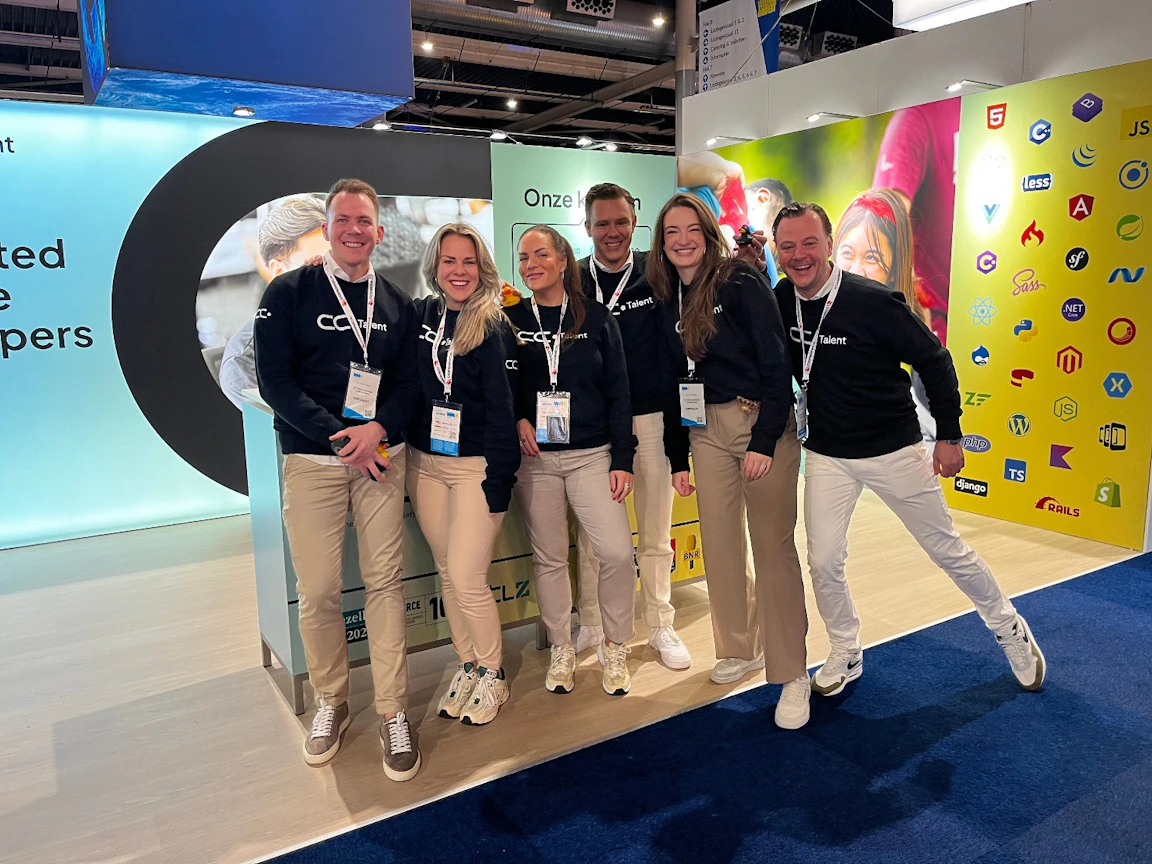 Six CC.Talent colleagues in branded sweaters and lanyards posing together at the company's event stand