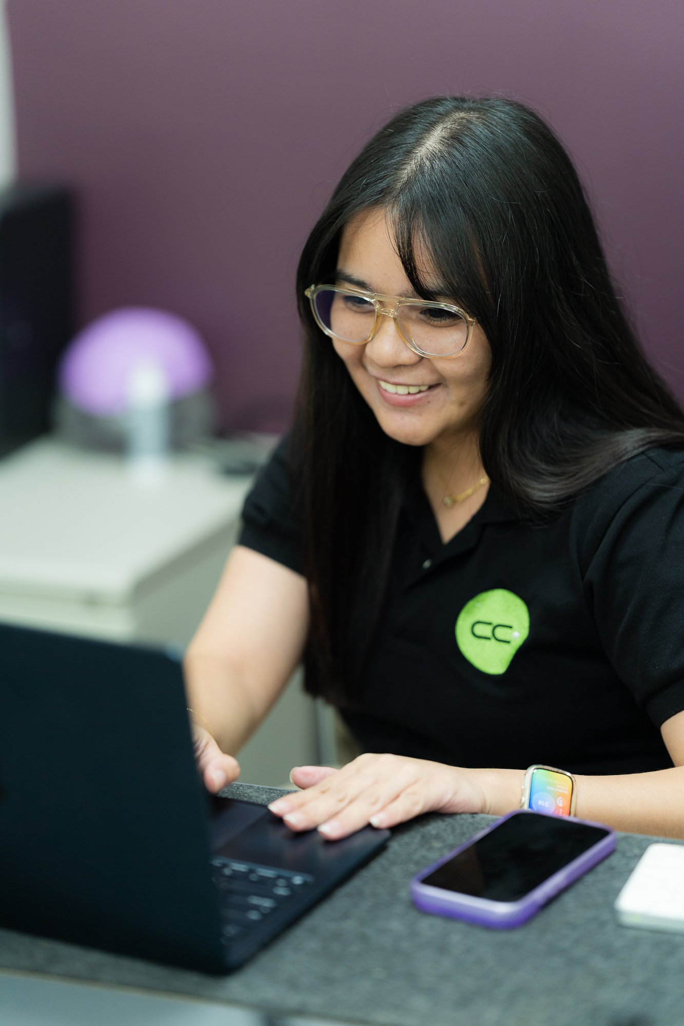 A CC.Talent finance professional in a branded polo shirt smiling while working at her laptop in the Manila office