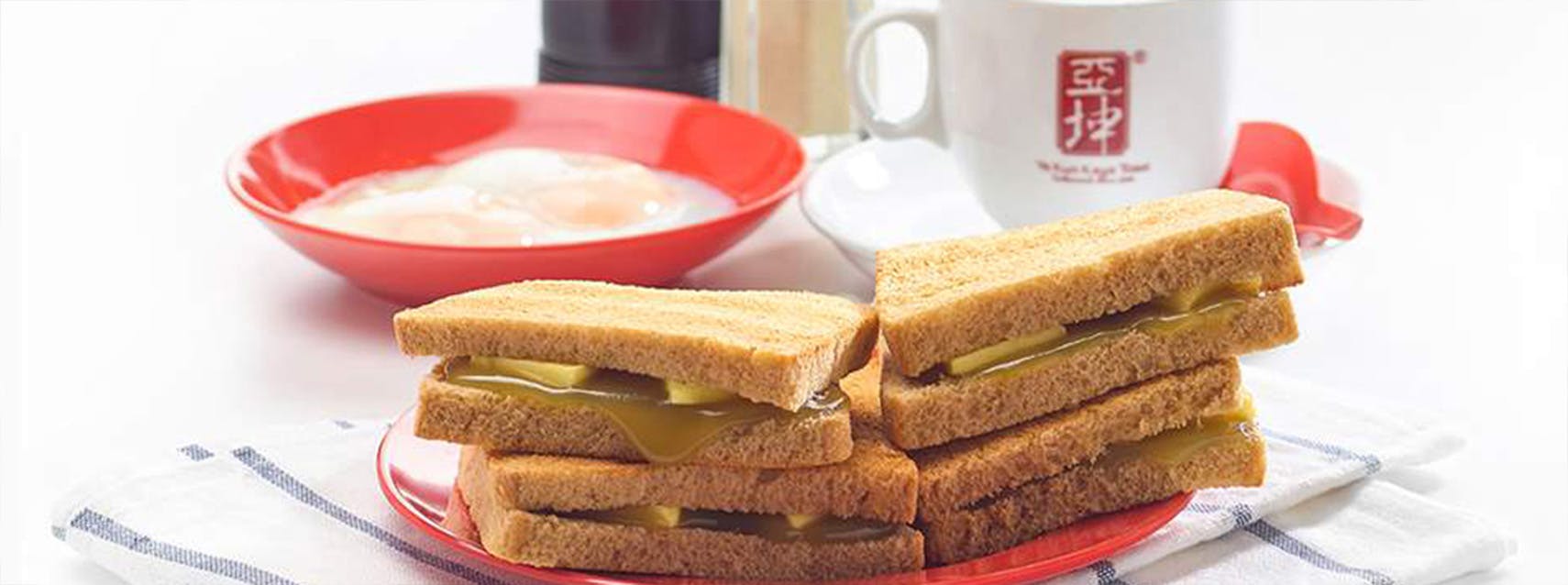 A bowl of two half-boiled eggs with black coffee and perfectly browned thin slices of bread, slathered in kaya and butter from Ya Kun Kaya Toast, close to 19 Nassim.