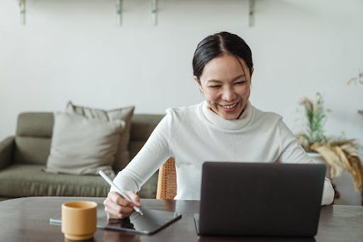 An Asian woman smiles as she works in a sleek, spacious home with modern furnishing, much like Sophia Regency will have.