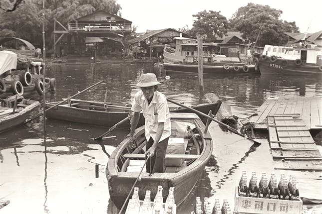 A black and white photo of a person in a boat at the Kallang River.